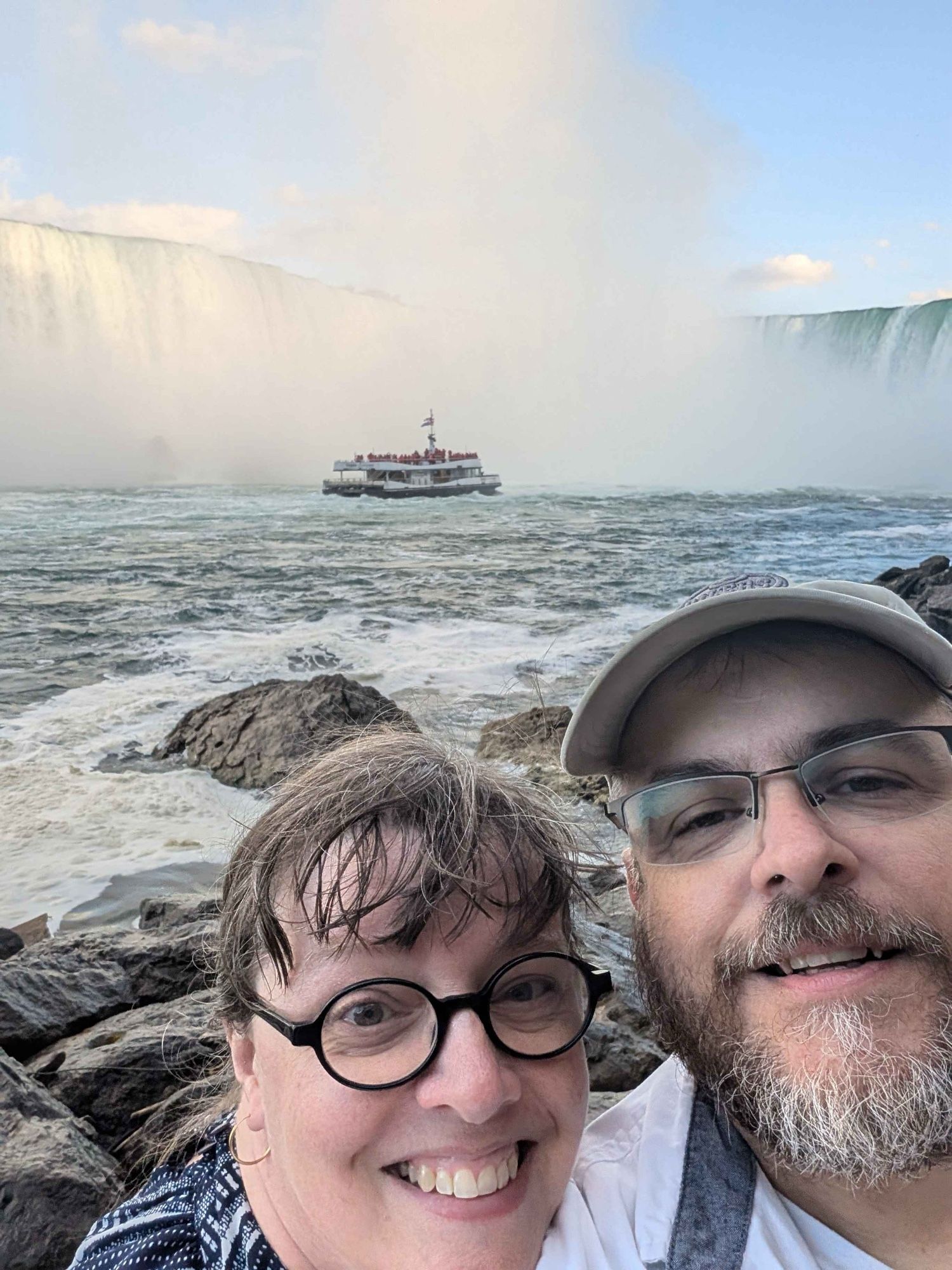 A middle-aged white couple stand on the platform at the end of the Niagara Falls Power Plant’s tunnel, where water once drained into the river after plunging through the hydroelectric power generating turbines near the water’s surface. A tourist boat (the Hornblower) can be seen approaching Horseshoe Falls (a high cliff completely covered in cascading water) in the background. Mist rises from the waterfall into a blue sky. This photo sounds like a white noise generator, but much louder - I bet the Thundering Ones don’t so much talk as shout at each other.