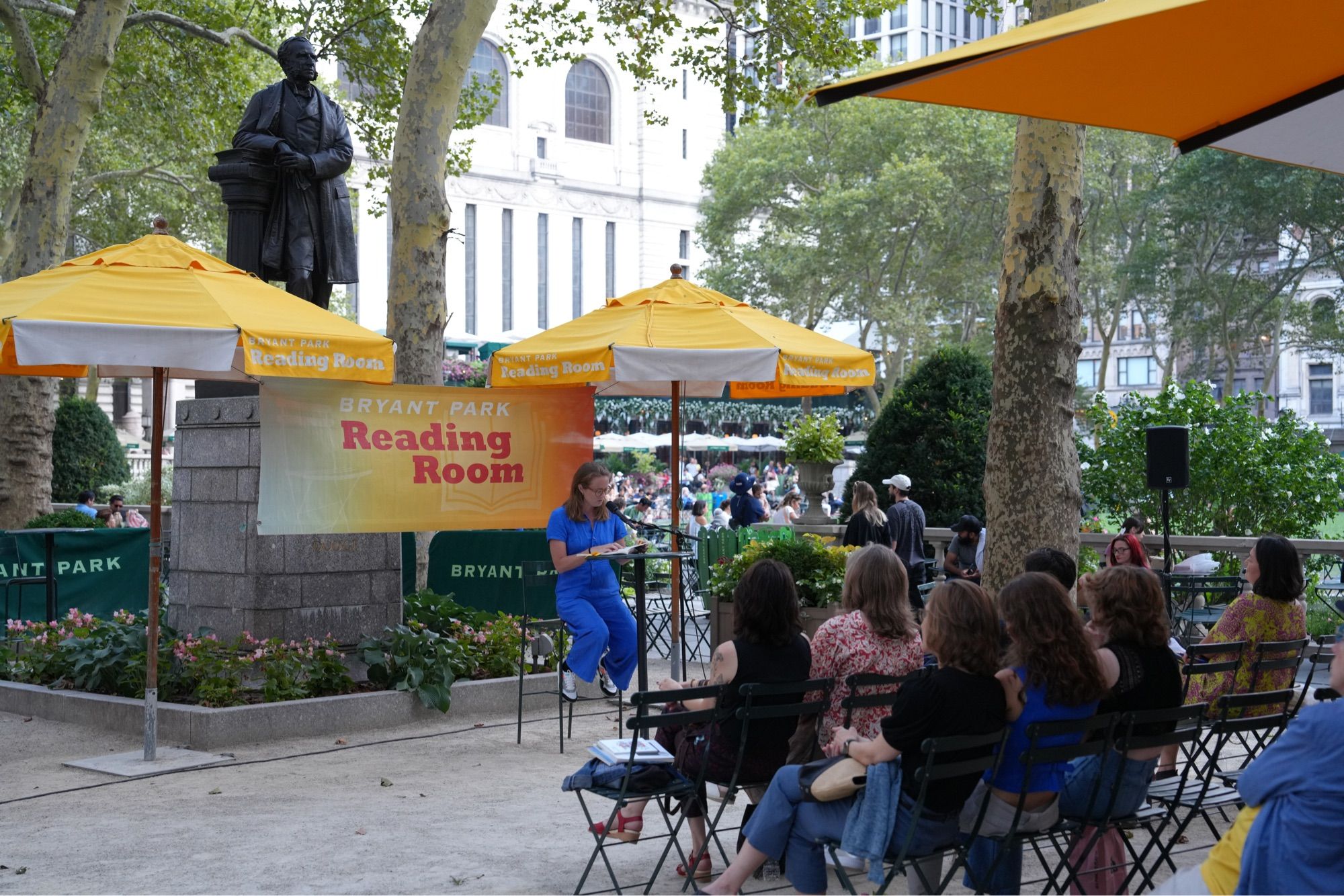 Me reading poems in a blue jumpsuit in the Bryant Park Reading Room