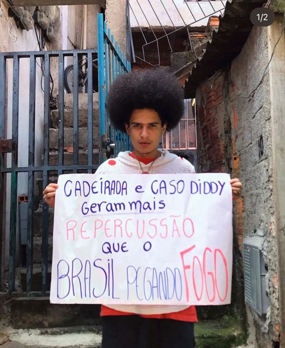 Poeta Cj segurando um cartaz que diz: “Cadeirada e caso Diddy geram mais repercussão que o Brasil pegando fogo”