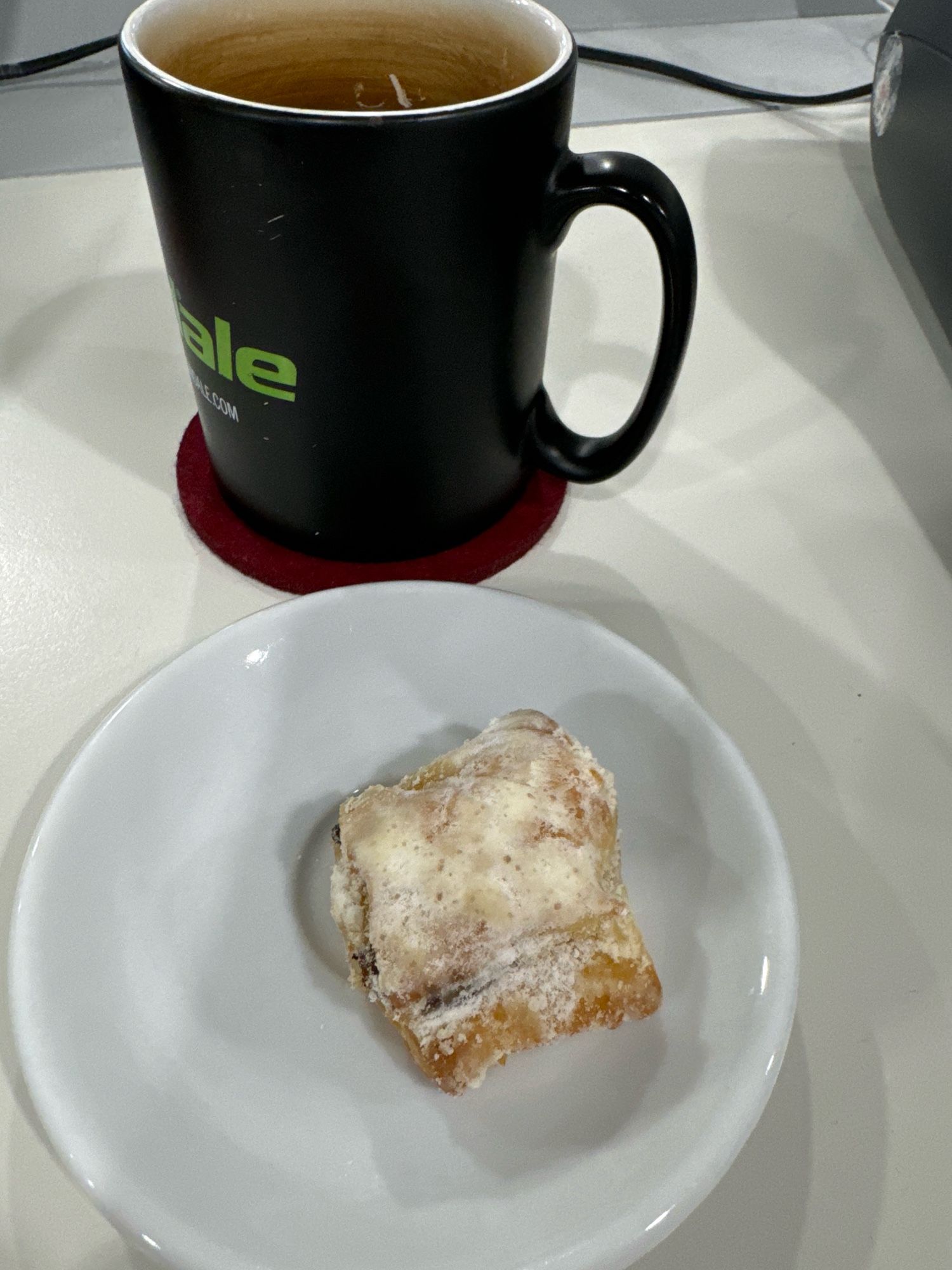 Ein kleines Stückchen Stollen auf einem weißen Tellerchen. Dahinter eine schwarze Kaffeerasse.