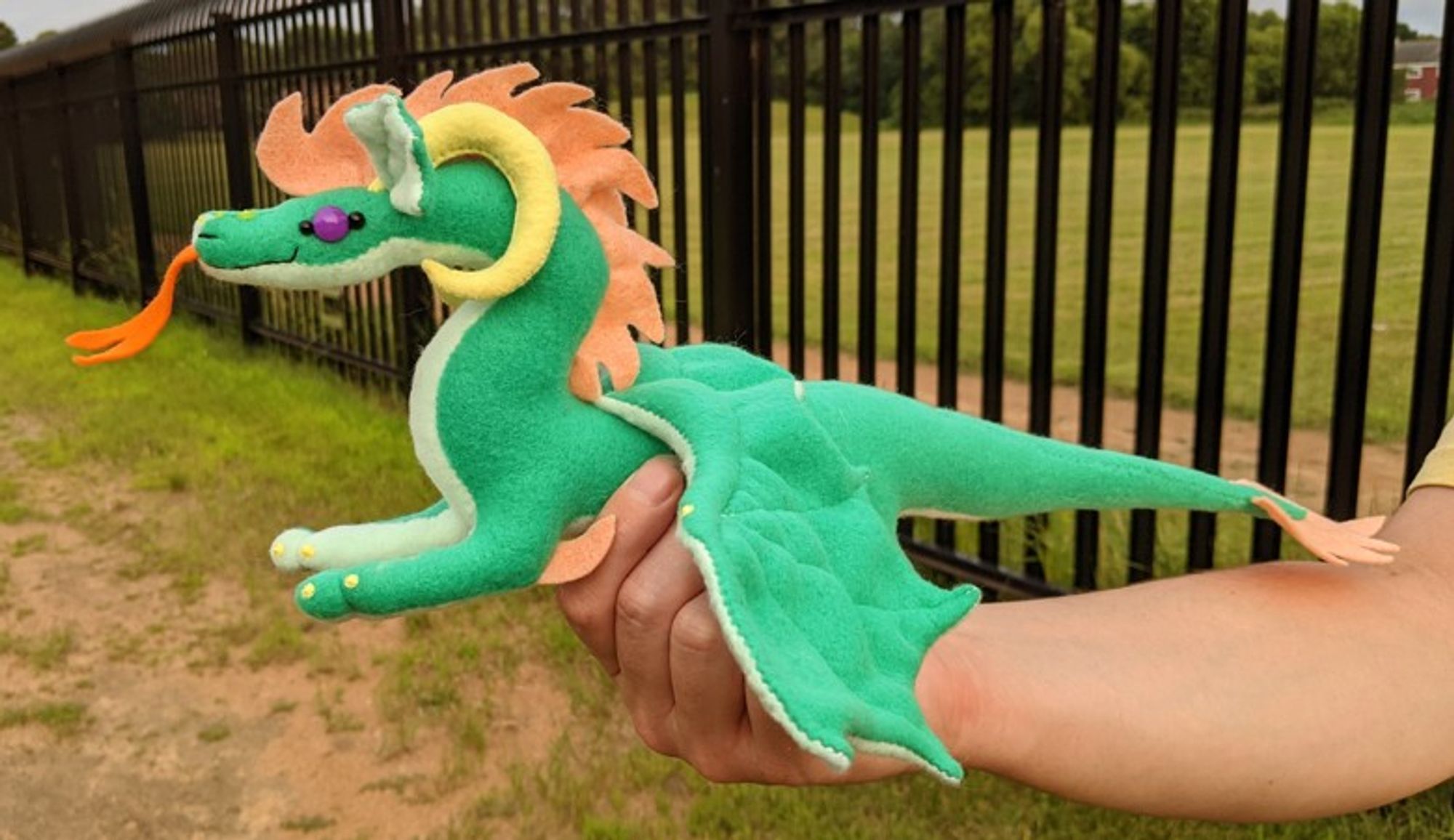 a bottle green dragon plushie with an light aqua underbelly/underwings/ears, a peachy-orange mane/crest and tailtip, yellow ram horns and claws, an orange tongue, and amethyst purple eyes