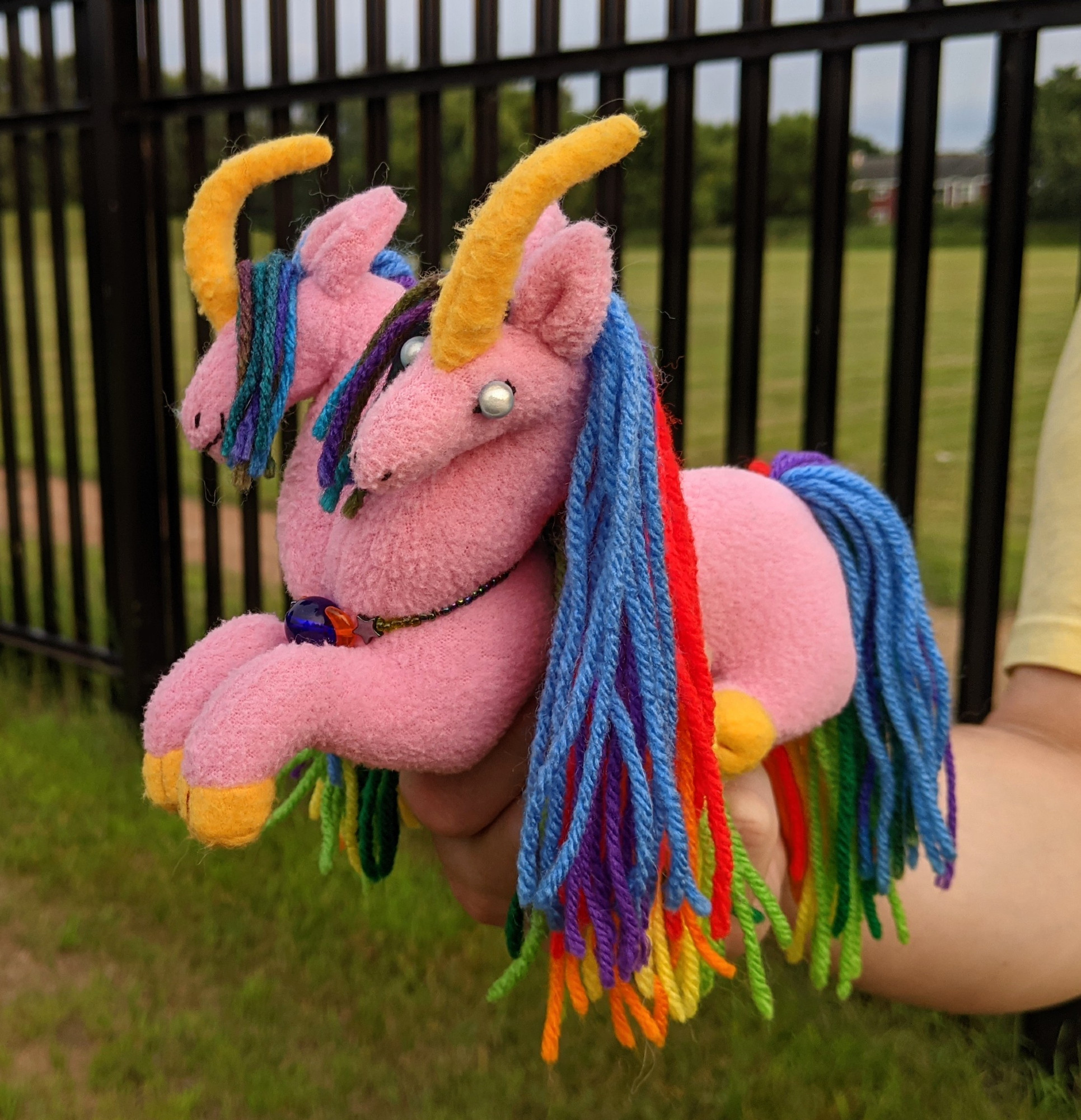 a pink 2 headed unicorn plushie with golden yellow horns & hooves, rainbow manes & tail, blue miracle bead eyes, and a necklace made from glass beads and hematite