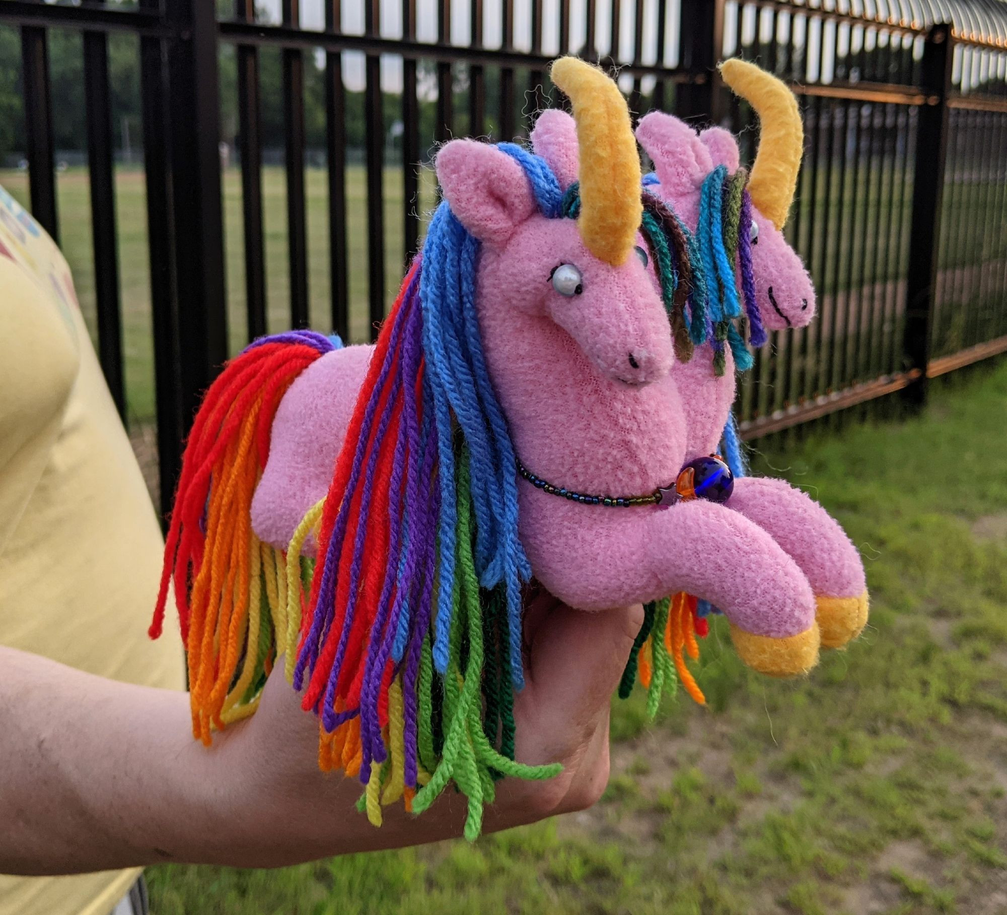 pink 2 headed unicorn plushie with golden yellow horns & hooves, rainbow manes & tail, blue miracle bead eyes, and a necklace made from glass beads and hematite