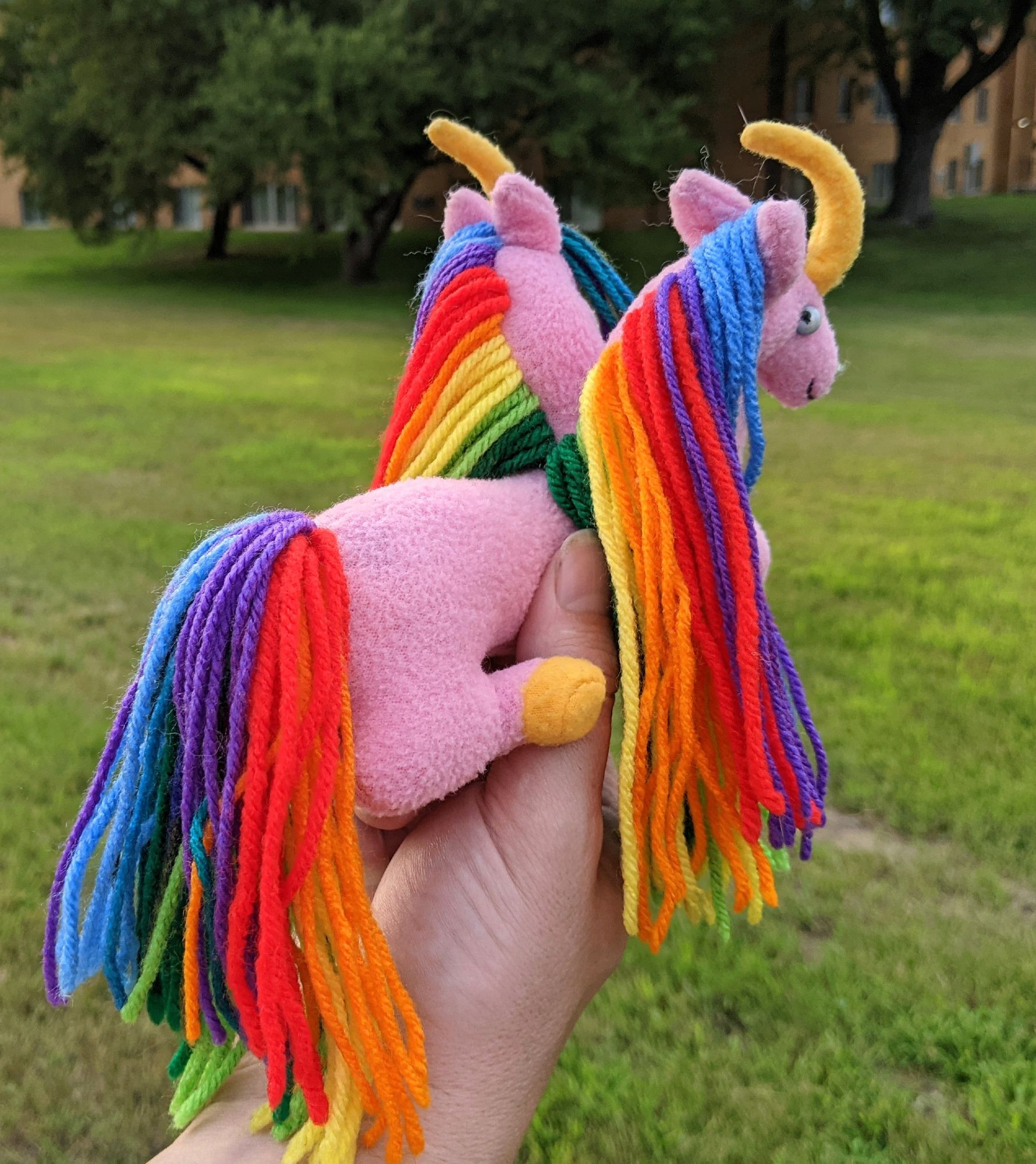 pink 2 headed unicorn plushie with golden yellow horns & hooves, rainbow manes & tail, blue miracle bead eyes, and a necklace made from glass beads and hematite