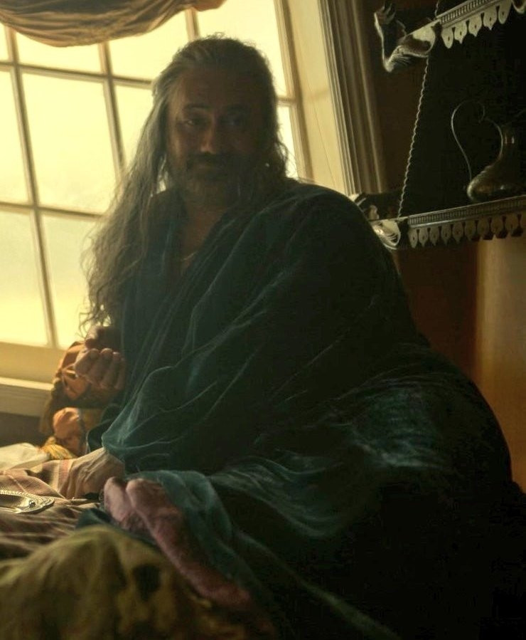 Ed Teach lounging in bed in the captains cabin in his luxurious teal blue robe, looking very satisfied.