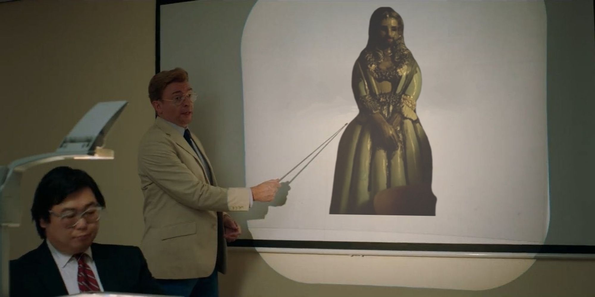 Rhys Darby's character from "Next goal wins" pointing to a projector screen where an image of  The Blackbeard cake topper bride has been inserted