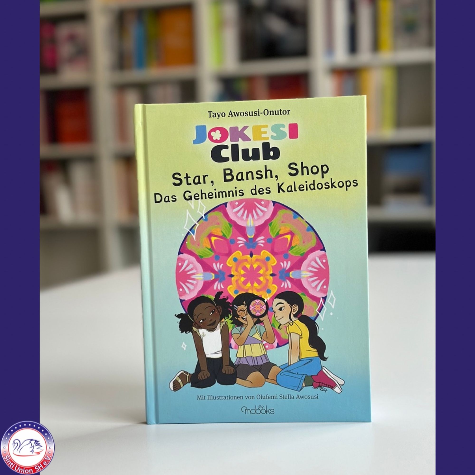 Das Buchcover zeigt das Kinderbuch „JOKESI Club: Star, Bansh, Shop – Das Geheimnis des Kaleidoskops“ von Tayo Awosusi-Onutor. Auf dem Cover sind drei Mädchen abgebildet, die zusammen auf dem Boden sitzen und neugierig in ein buntes Kaleidoskop blicken. Die Illustration ist lebhaft und farbenfroh, mit einem Kaleidoskop-Muster im Hintergrund. Es wird auch erwähnt, dass die Illustrationen von Olufemi Stella Awosusi stammen.