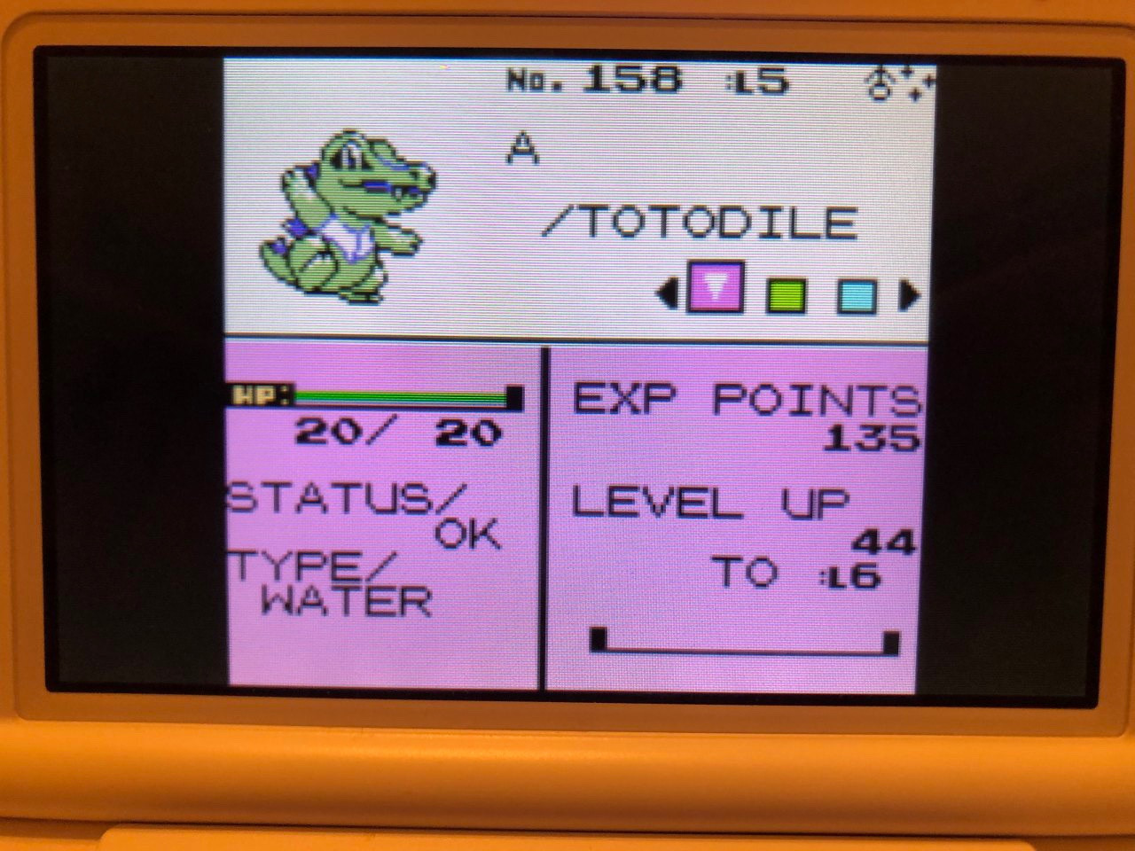 a 3ds screen showing a level 5 shiny totodile in pokemon crystal’s virtual console. the shiny totodile’s name is ‘A’ and he is a minty green colour with purple spikes on his back, a purple mouth, and purple detailing on his chest and around his eyes. 