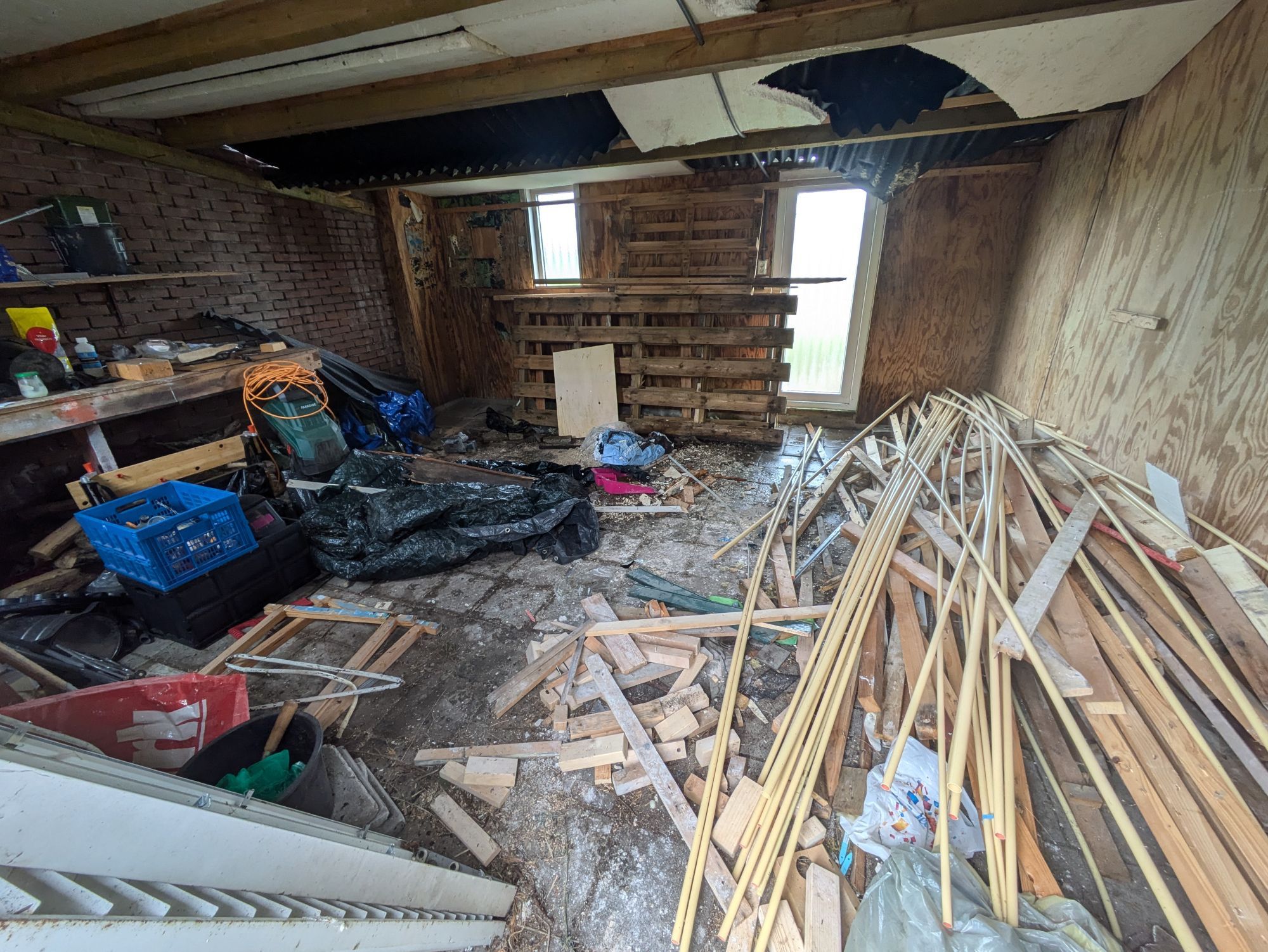 wide-angle shot of the shed this time. there's still a big pile of wood (and PVC electrical conduit), but most of the other garbage is gone now. the other side has two tarps, various crates and things, a wood chipper, a light fixture...