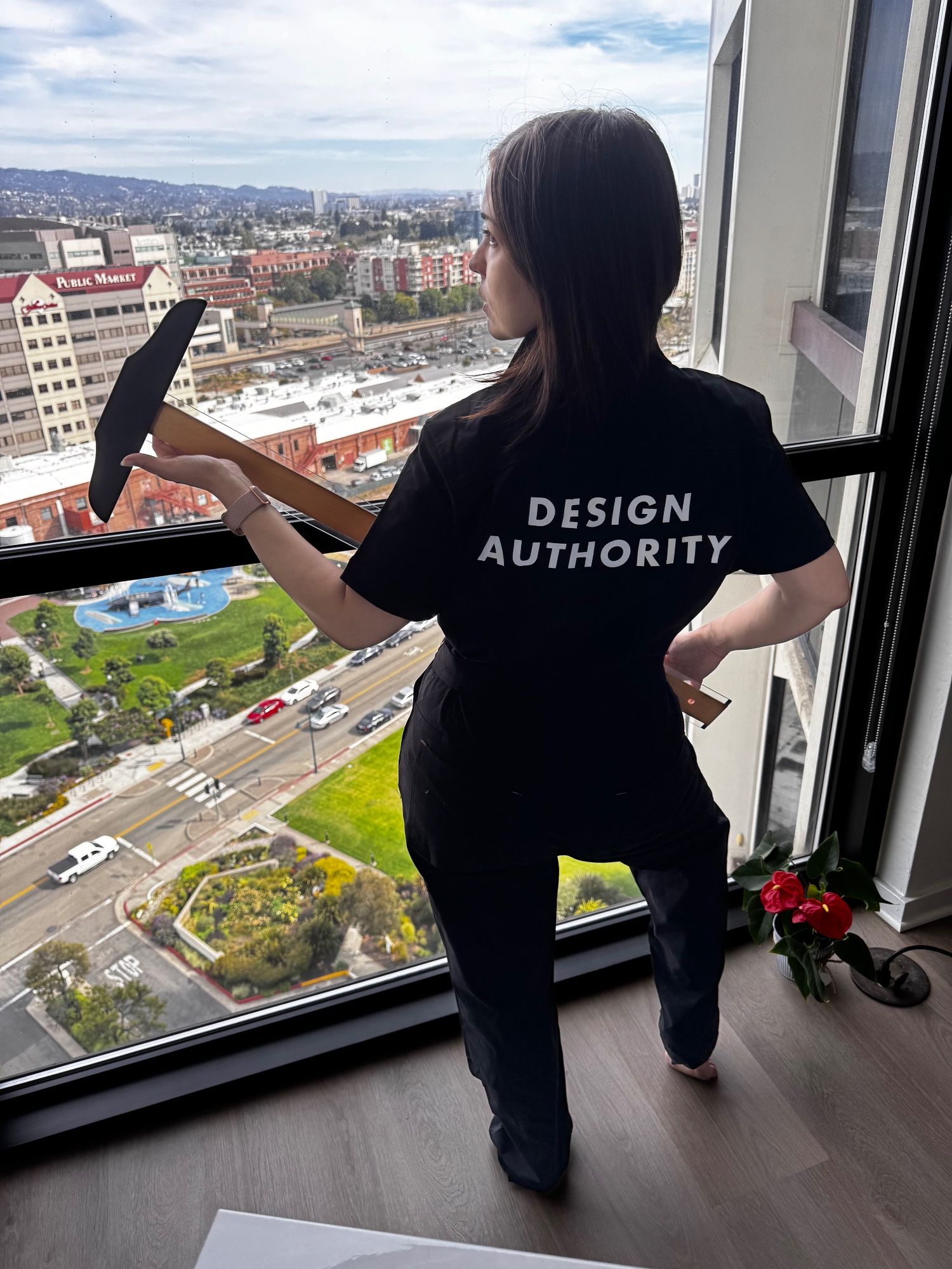 Renée stands by a hire-rise window overlooking Emeryville, T Square in hand, wearing a Design Authority jumpsuit like Adam Driver's lackeys in the extremely popular hit movie Megalopolis