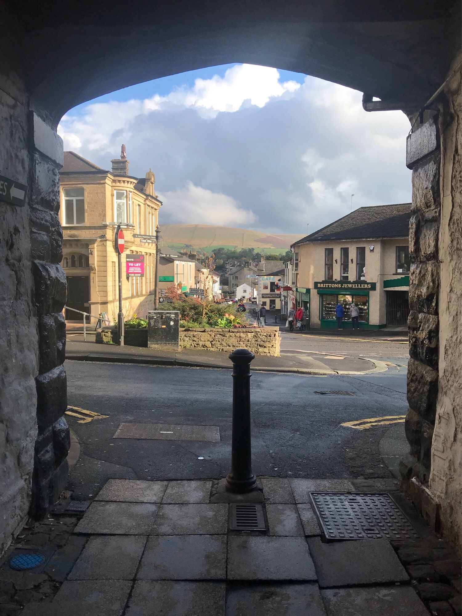 View from an arched passageway: some shops and in the distance a hill - glorious Pendle Hill - beneath cloudy blue skies.