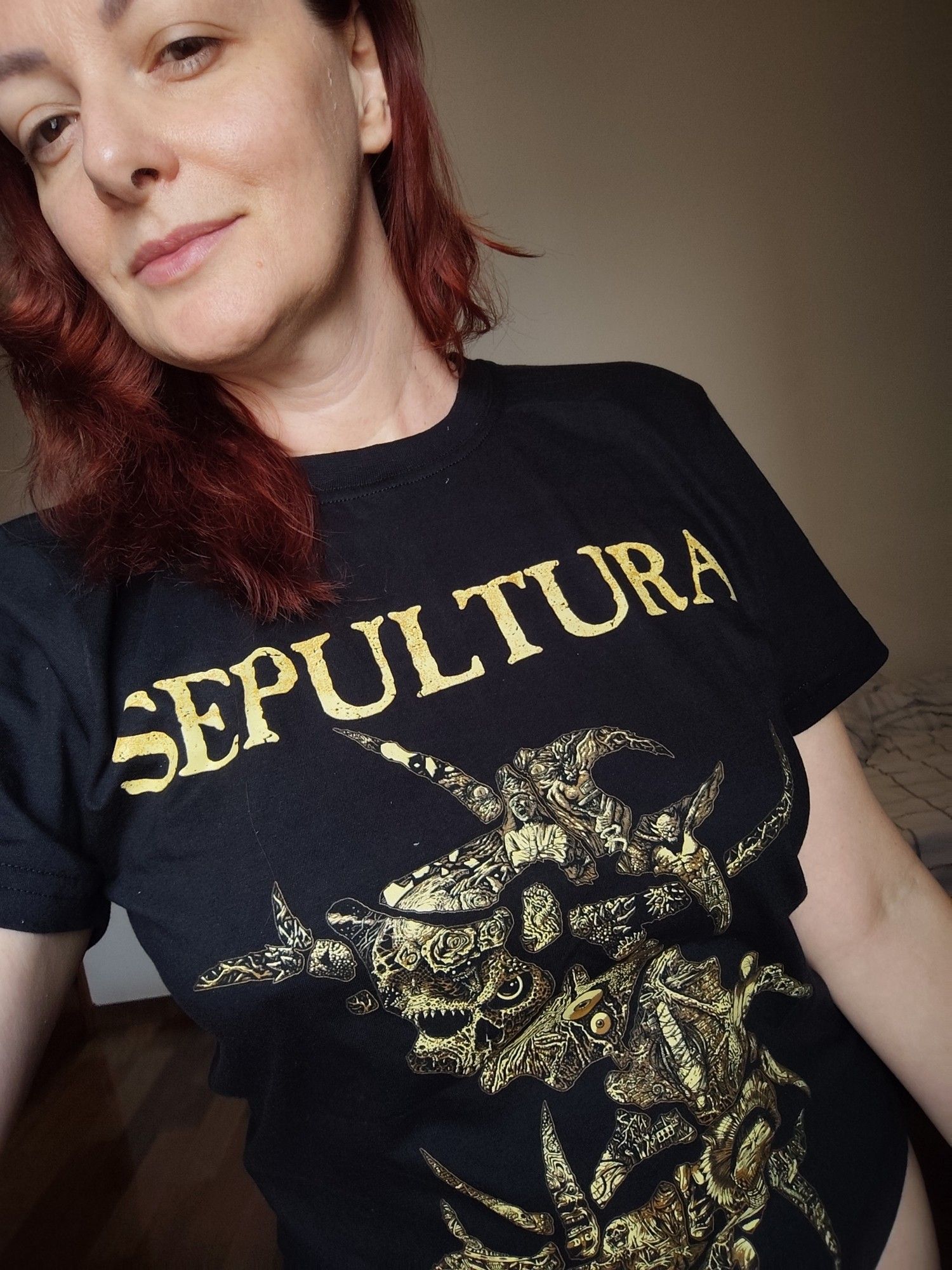 Eu - mulher branca de cabelos pintados de vermelho - usando uma camiseta preta com estampa em dourado da banda Sepultura.