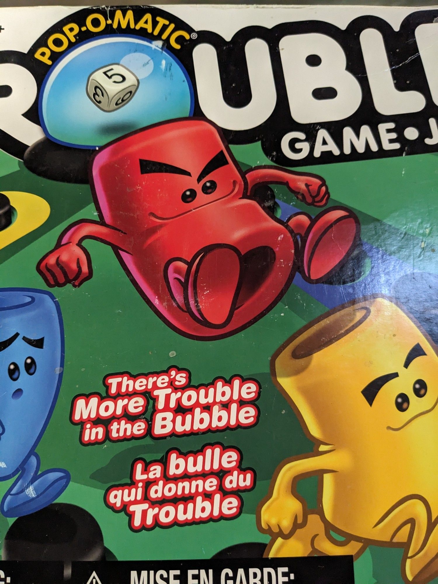 Photo of the box cover for Trouble, the board game. The little hollow pieces are depicted in an anthropomorphic fashion, and the red guy is jumping on the yellow guy (as one does). It did, however, give us direct insight into these pieces' apparently gaping assholes.