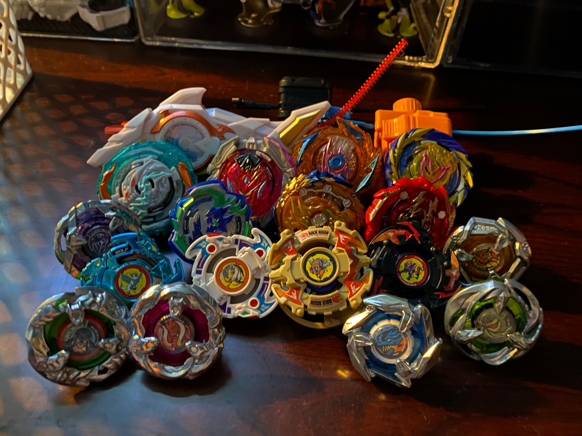 17 Beyblades on a desk, in order from back to front, left to right they are Zeal Nydhogg (Burst), Xiphoid Knight (Burst), Demise Hyperion (Burst), Fierce Achilles (Burst), Helm Knight (X), Ogre 05 (Burst), Wizard Fafnir (Burst), Bushin Ashindra (Burst), Tail Viper (X), Wolborg (Bakuten Shoot), Dragoon F (Bakuten Shoot), Rock Bison (Bakuten Shoot), Flash Leopard 2 (Bakuten Shoot), Yell Kong (X), Tusk Mammoth (X), Dagger Dran (X), and Gale Wyvern (X)