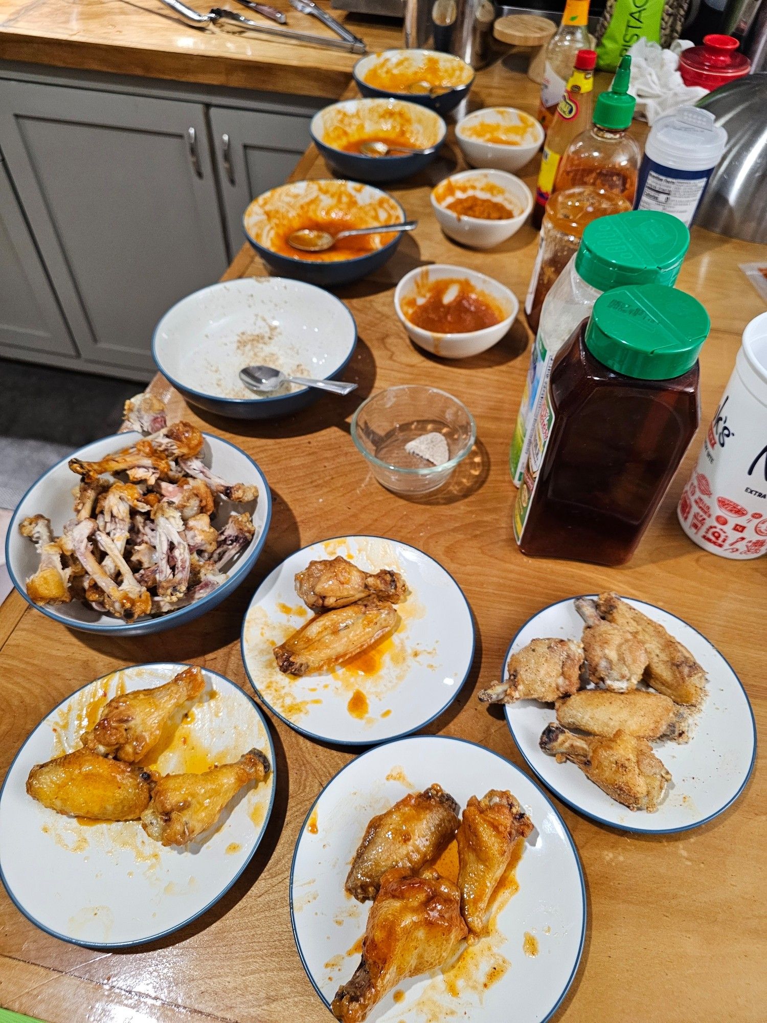 Photo of a kitchen counter with many bowls and sauces and plates of hot wings arrayed throughout.