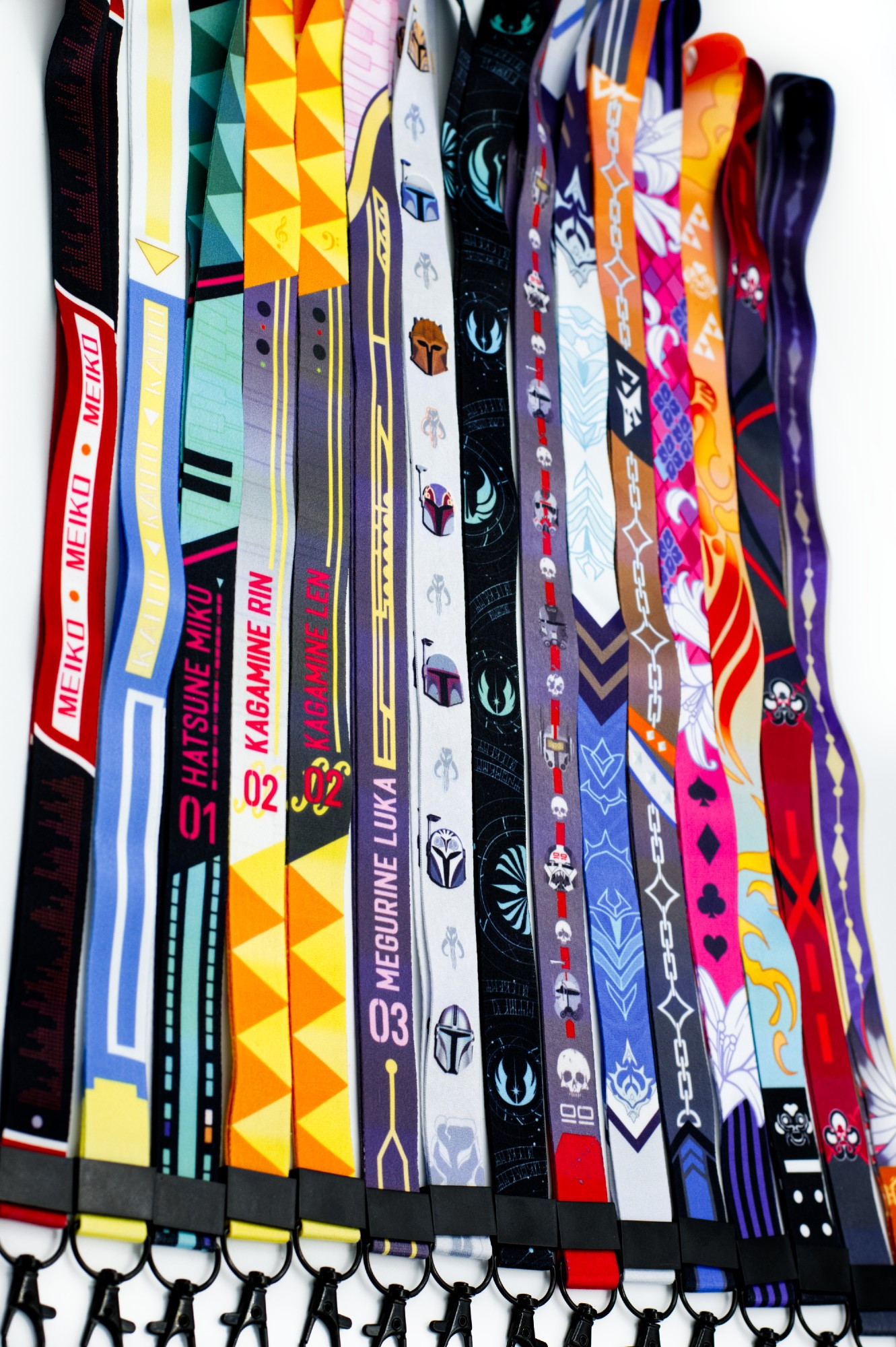 Photo of a lineup of 15 lanyards. Left to right: MEIKO, KAITO, Hatsune Miku, Kagamine Rin, Kagamine Len, Megurine Luka, Mandalorians, the Jedi Code, the Bad Batch, Regis Altare, Axel Syrios, Gavis Bettel, Josuiji Shinri, Machina x Flayon, Banzoin Hakka