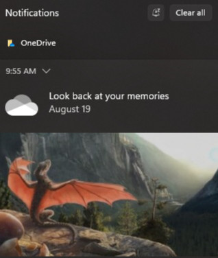 a screenshot of a Windows 11 notification from OneDrive reading "Look back at your memories - August 19" followed by a picture of a dragon hatchling perched on a cliff's edge overlooking a pristine mountain valley at sunrise. this actually happened to me