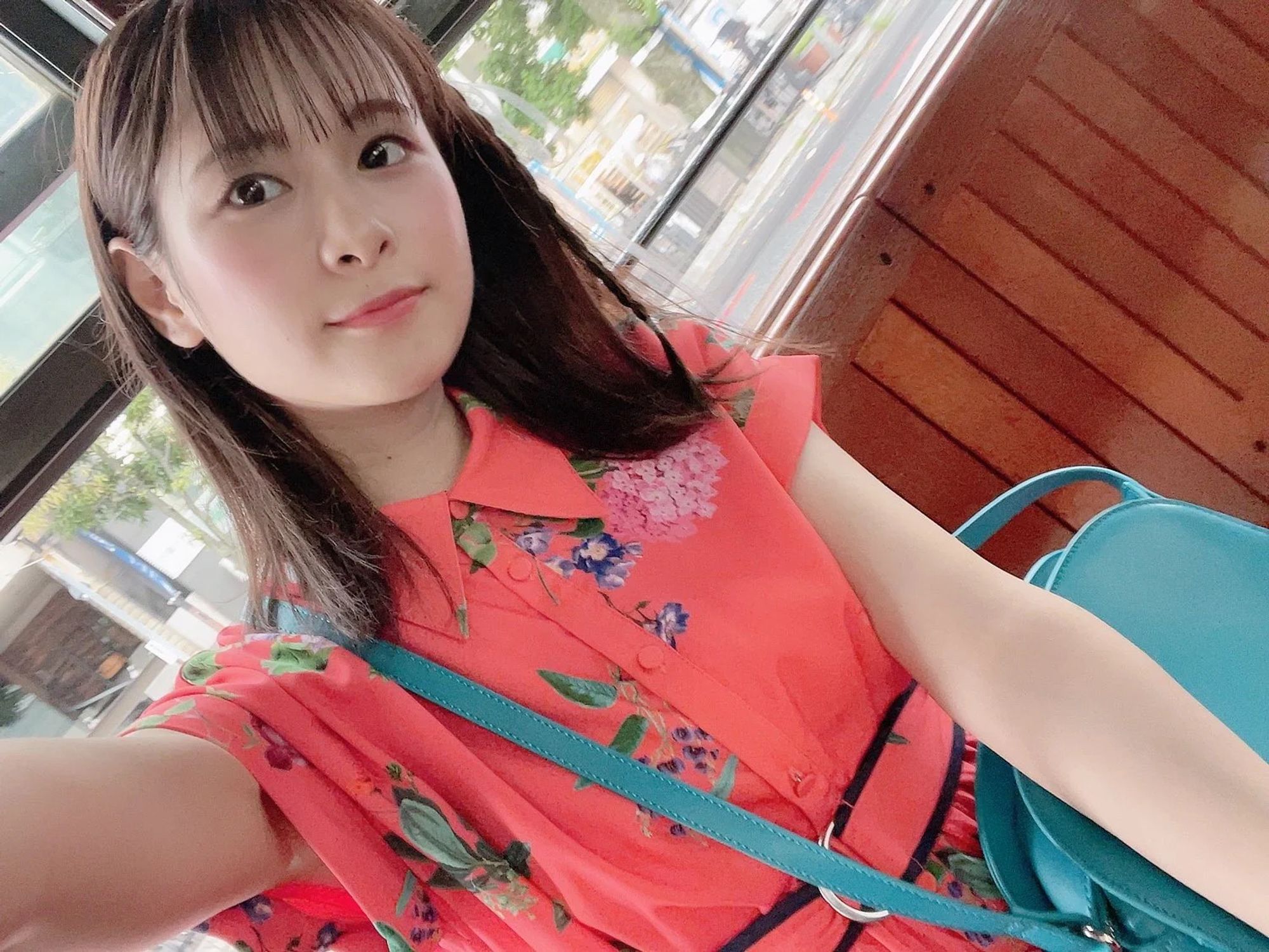  Kaori smiling wearing a red blouse with flowers with a teal handbag on her shoulders.