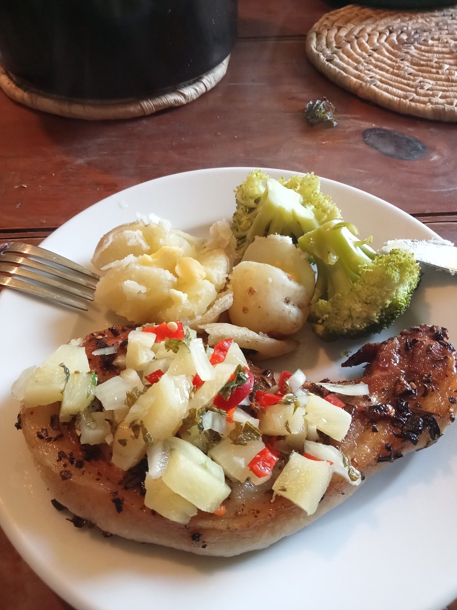 Pork chop covering pineapple and chilli, with pototoes and broccoli on a plate