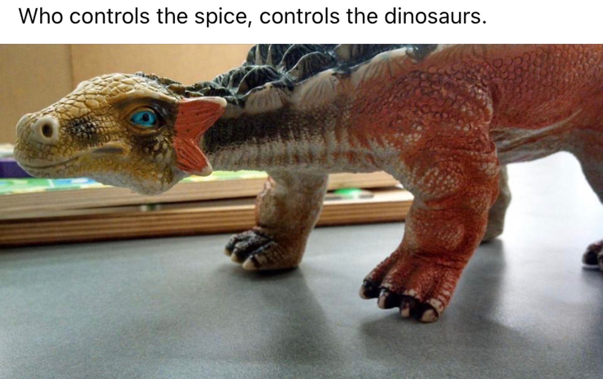 Image of toy dinosaur with vivid blue eyes, captioned “Who controls the spice, controls the dinosaurs.”