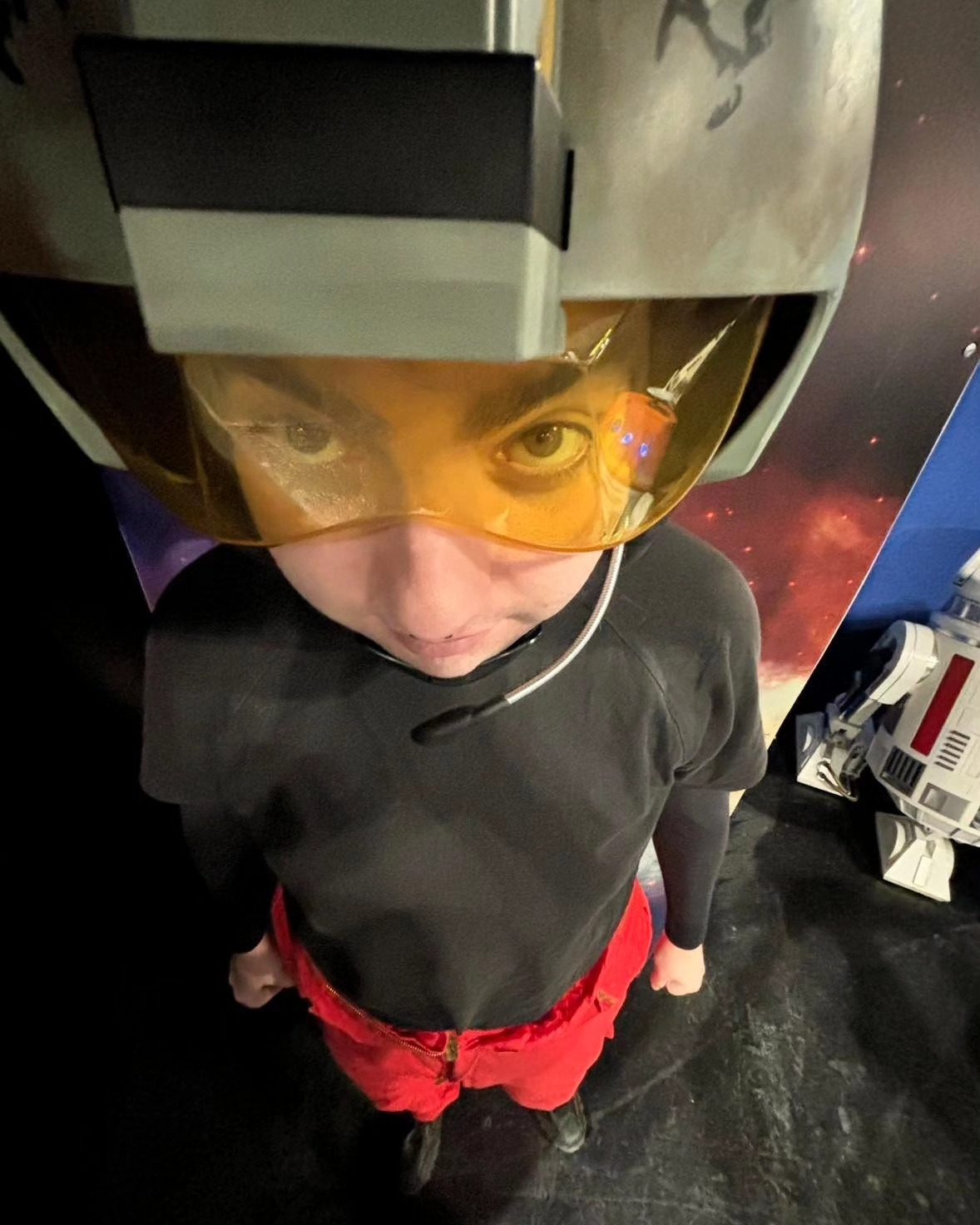 0.5 close up photo of Josie in an X Wing pilot cosplay with a R5 droid in the background