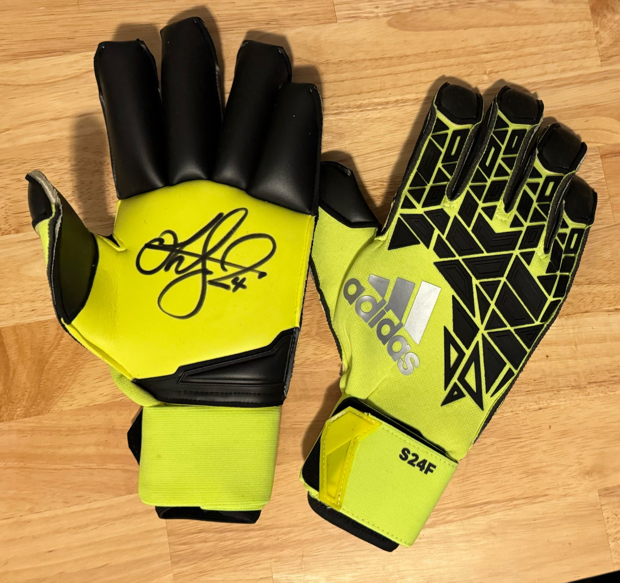 A bright yellow pair of Adidas goalkeeper gloves autographed by Stefan Frei. S24F is printed on the cuff of each glove.