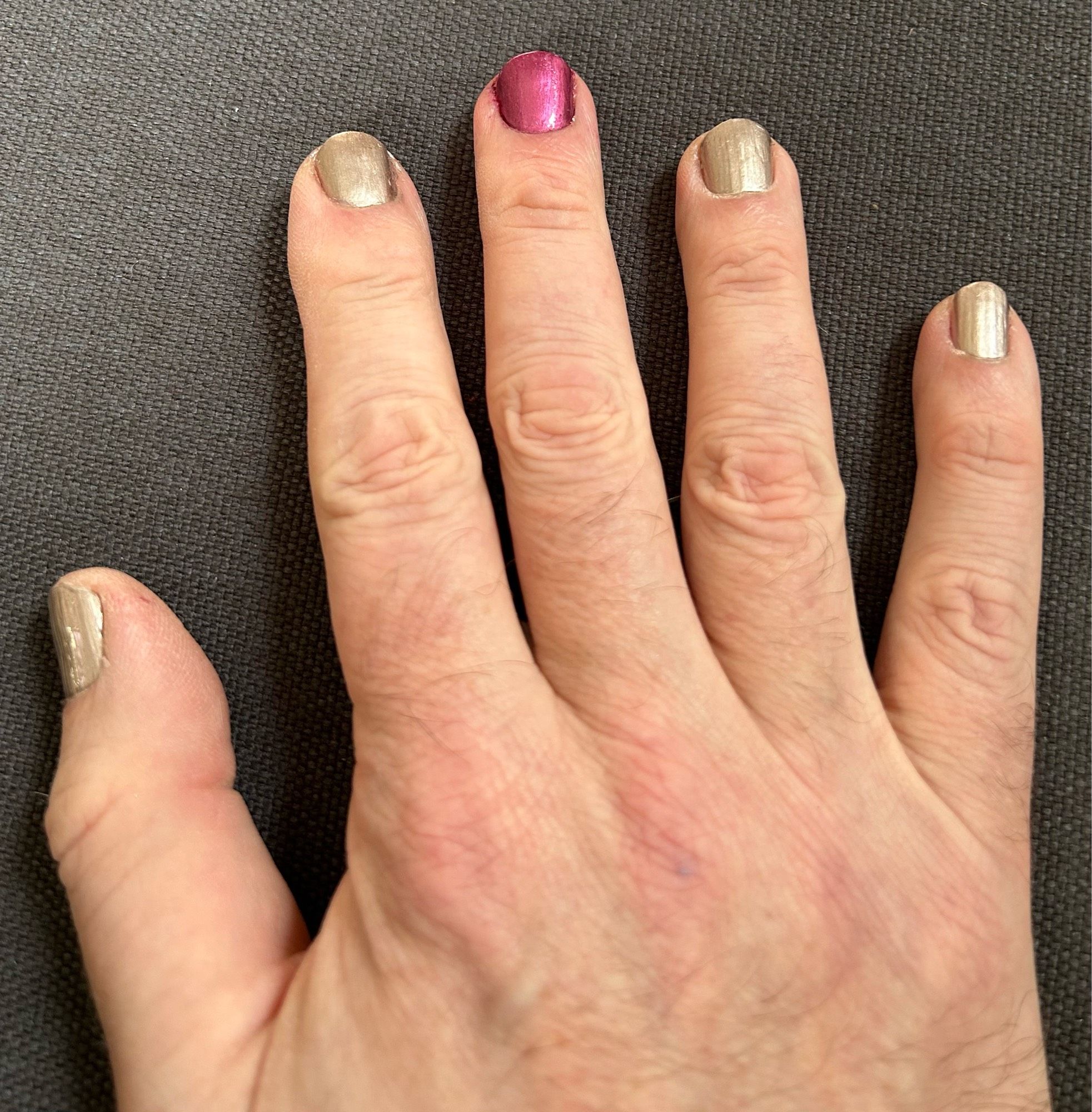 You can see s right hand with painted fingernails that is resting on a grey cloth background. The middle finger is painted in red, the four others in a kind of silverish rosé.