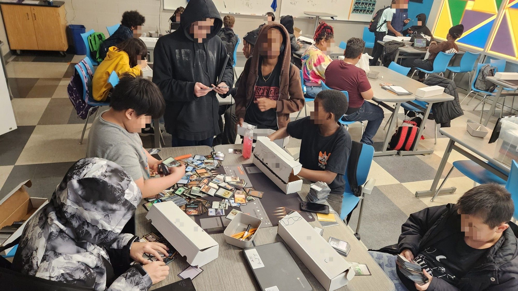 A classroom full of students playing games and sorting Magic cards.