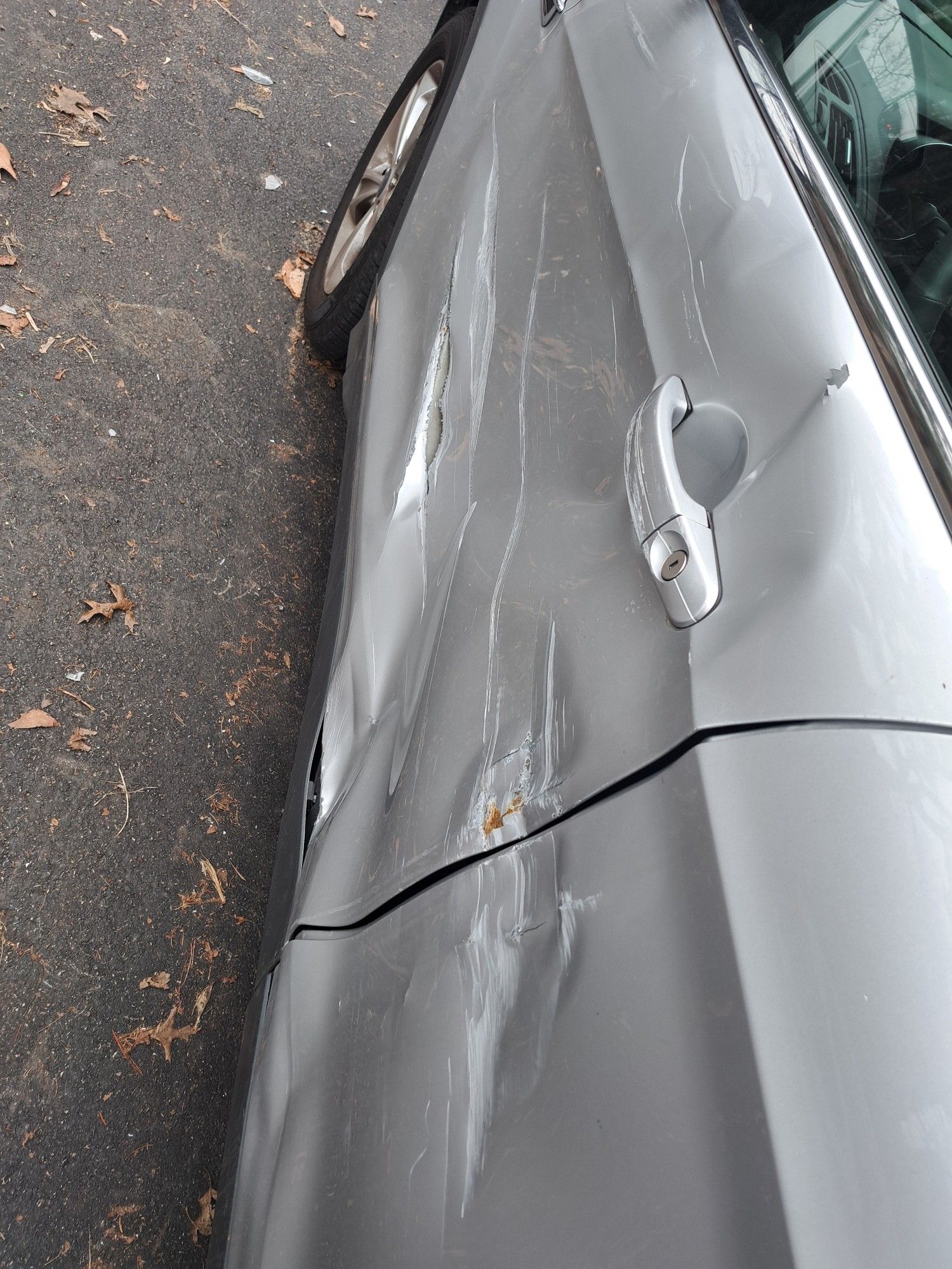 The side of a silver car showing extensive damage.