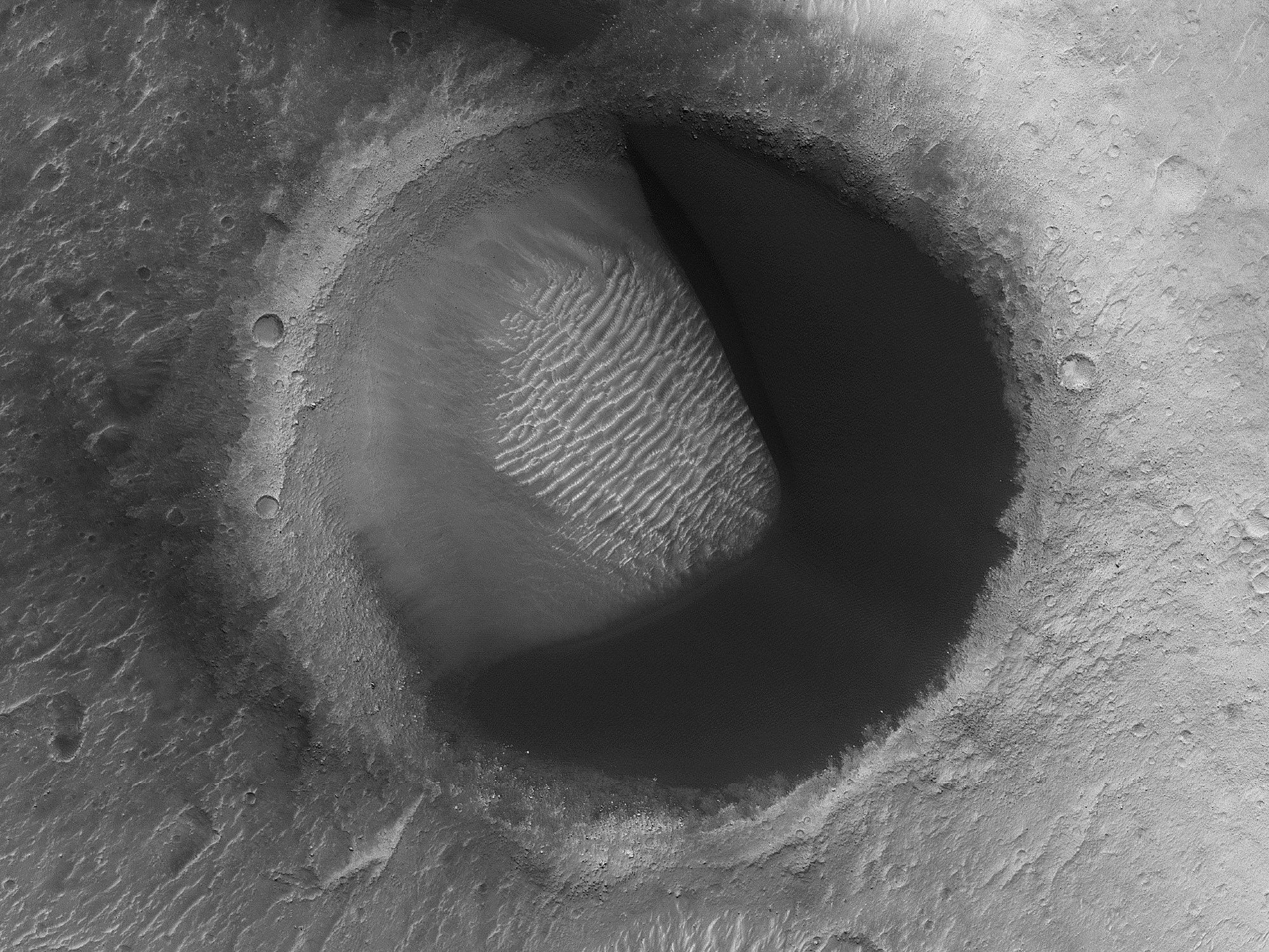 Image shows a dark dune field within one side of an impact crater that gives it the shape of the popular video game character Pac-Man. (NASA/JPL-Caltech/University of Arizona)