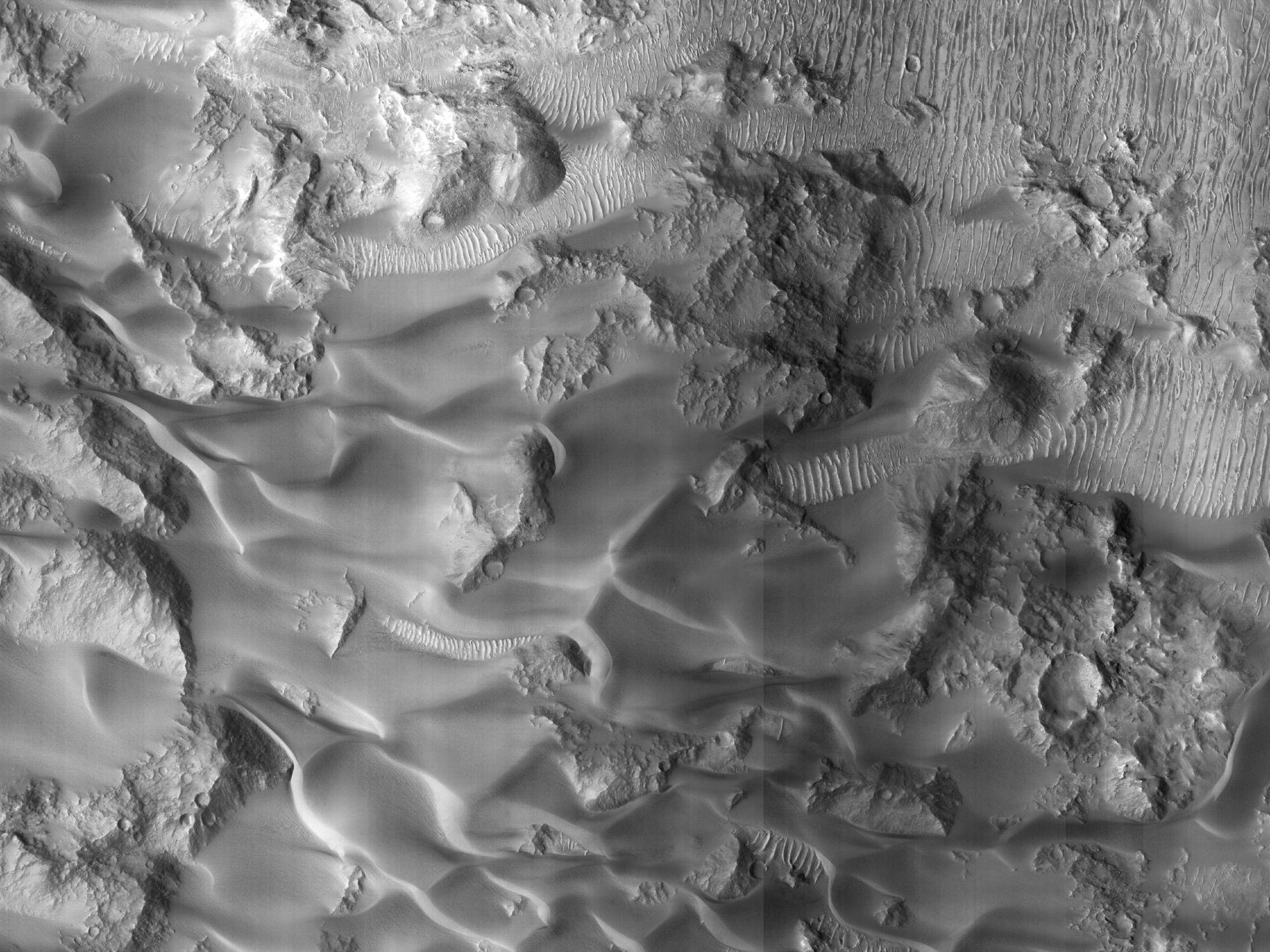 Image shows rocky outcrops surrounded by large dune sheets that are darker in color. There are also lighter-toned dunes with prominent crests. (NASA/JPL-Caltech/University of Arizona)