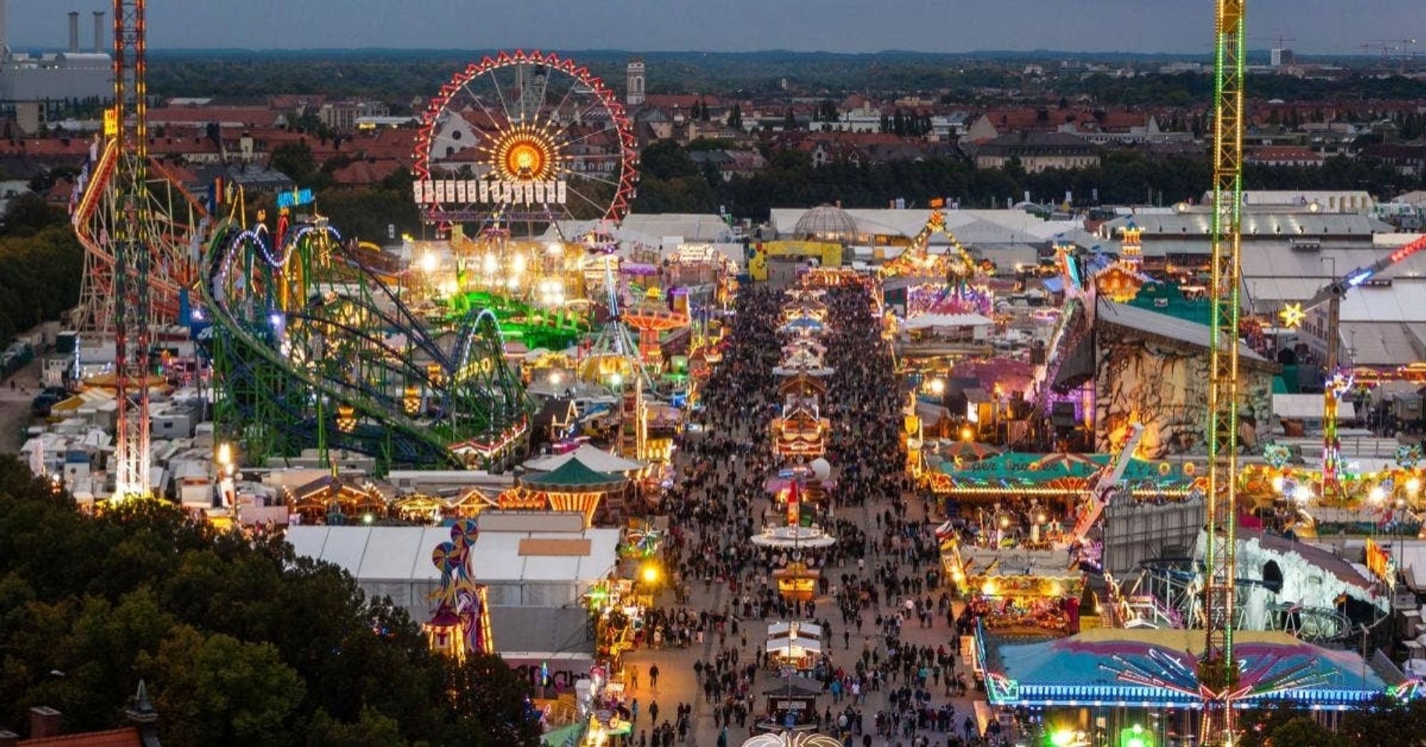 Ein Bild vom Oktoberfest. Es sind haufenweise leute zu sehen. Daneben Achterbahnen und Riesenräder