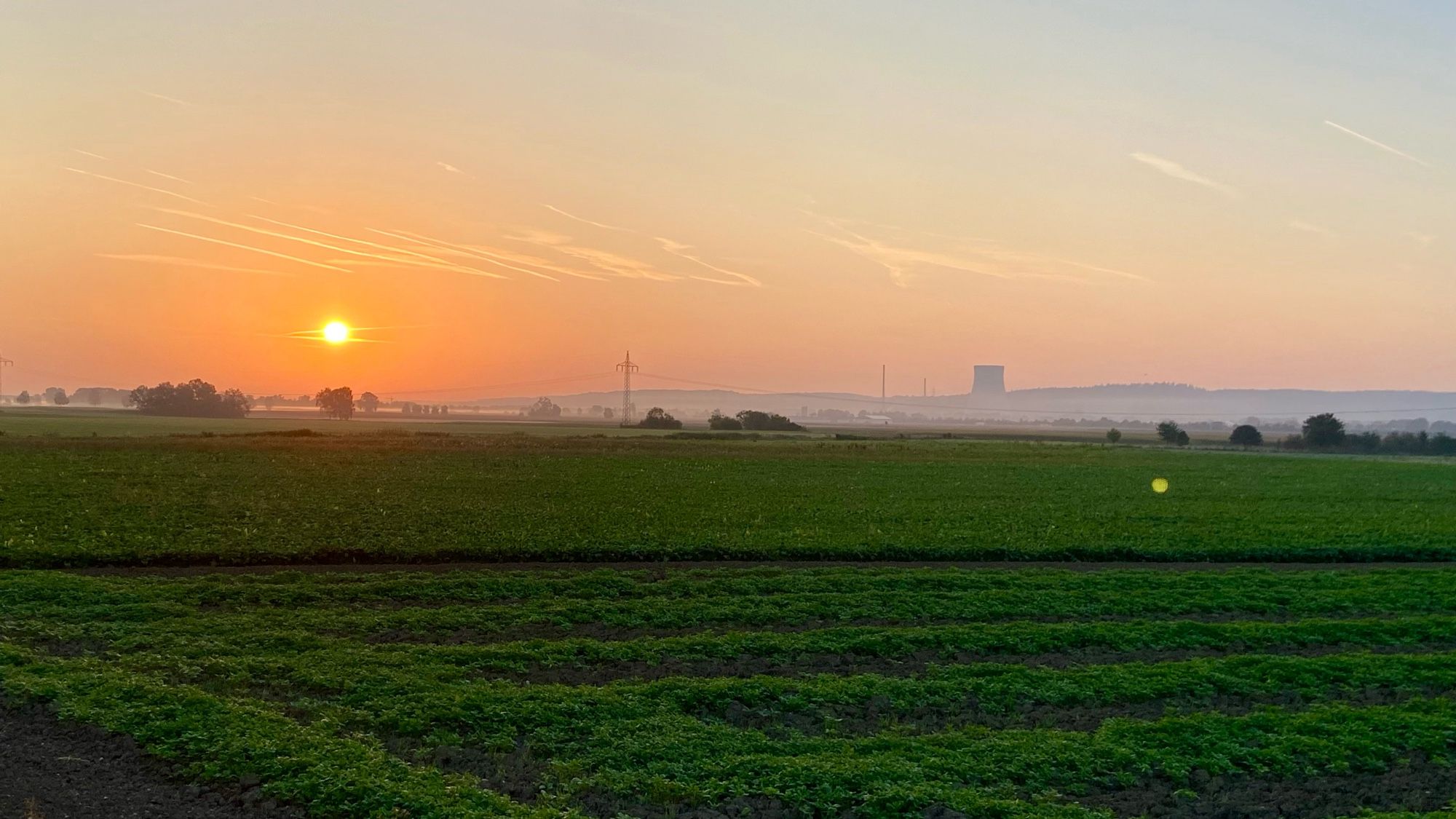 Sonnenaufgang über Ohu2, dem letzten stillgelegten AKW in Deutschland. Im Vordergrund grüne Felder.