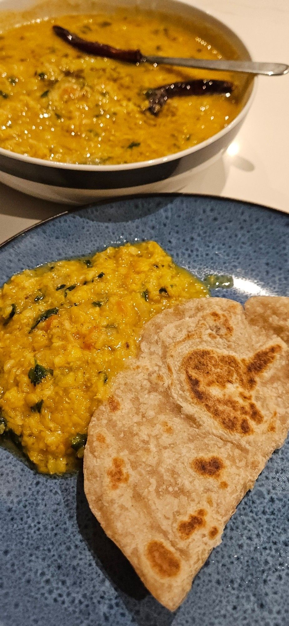 Portrait: paratha and homemade dal on a blue plate, with a bowl containing more dal in the background