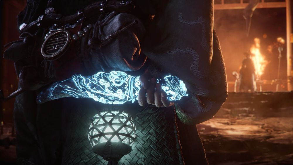 A screenshot from the Woochi the Wayfarer reveal trailer showing the back of the protagonist with a teal orb lit up while holding a girthy blade, lit in neon light blue. In the background, ahead of the protagonist, is a large fire with a shaman woman standing in front of it menacingly. 