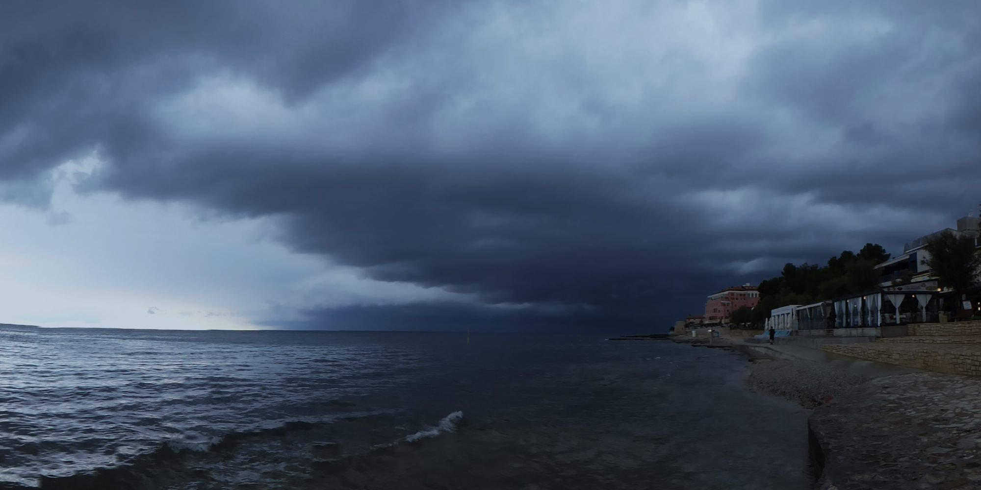 das bild zeigt eine ansicht der südküste  der stadt novigrad in istrien/kroatien mit blickrichtung west. dunkle wolken hängen drohend über der stadt, die wenig später durch heftigen regen überschwemmt wurde.
windboe und wellengang kamen erst später dazu.