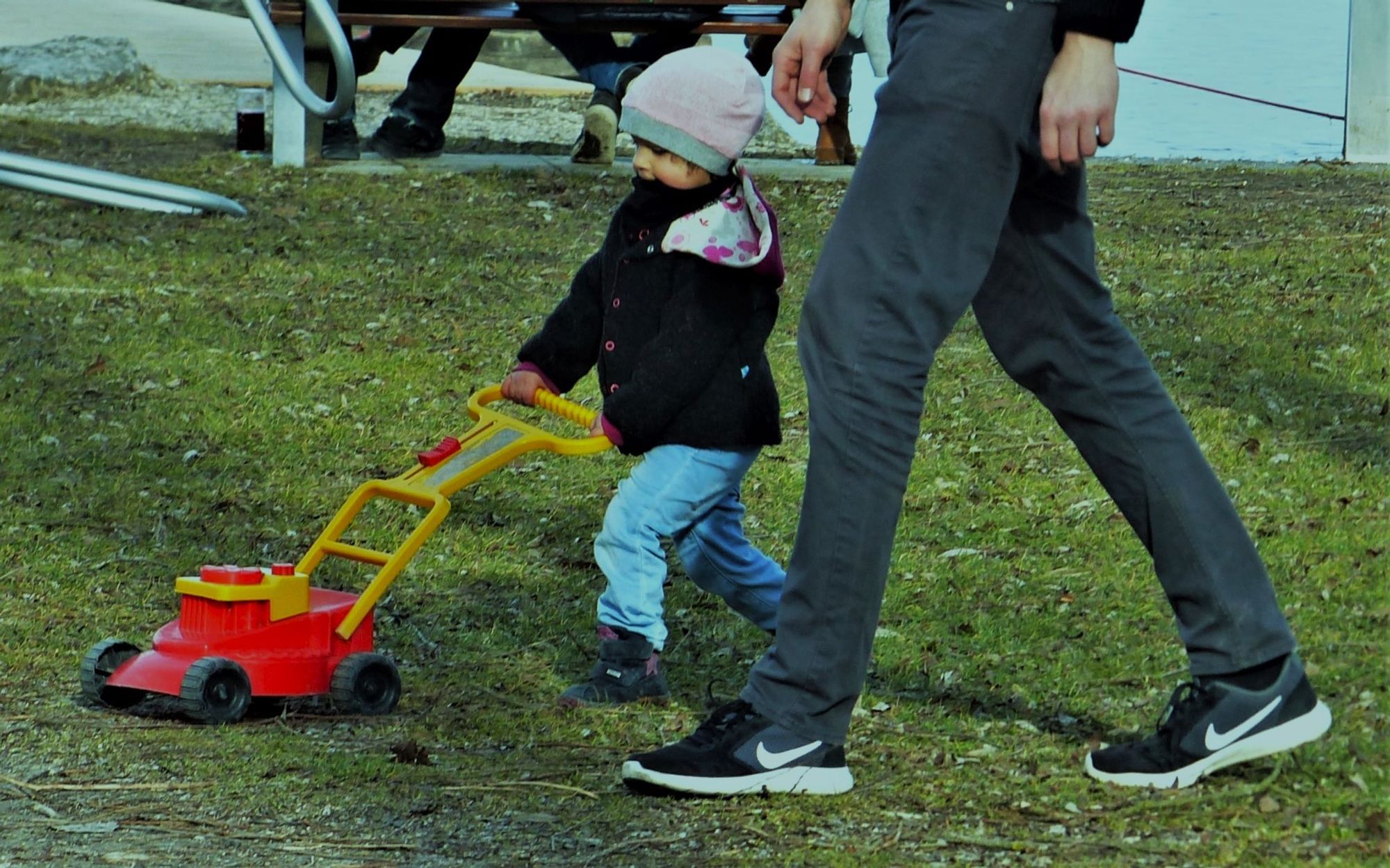 das bild zeigt einen fröhlichen kleinen jungen, der mit seinem vater im park spazierengeht. es ist kurz n. weihnachten, ziemlich kalt und  trotzdem wollte der kleine seinen spielzeugrasenmäher aus k´stoff mit zum ausflug nehmen. voller stolz  schiebt er ihn vor sich hin, so wie er es von papa im sommer sah .