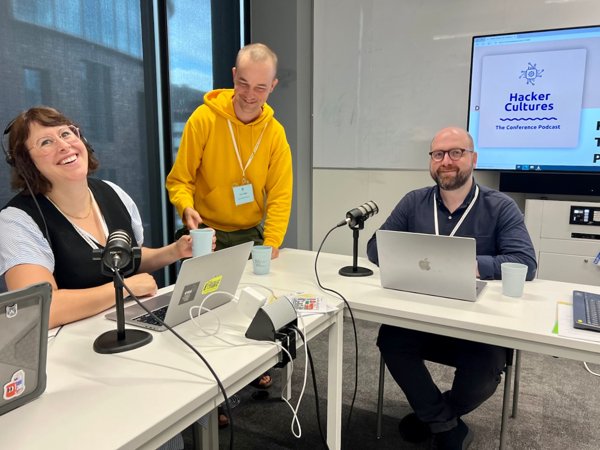 Hosts Paula Bialski, Mace Ojala and guest Charles Berret at the #EASST4s2024 conference. They are sitting at tables with the microphone sinfront of them just before the start of the podcst panel.