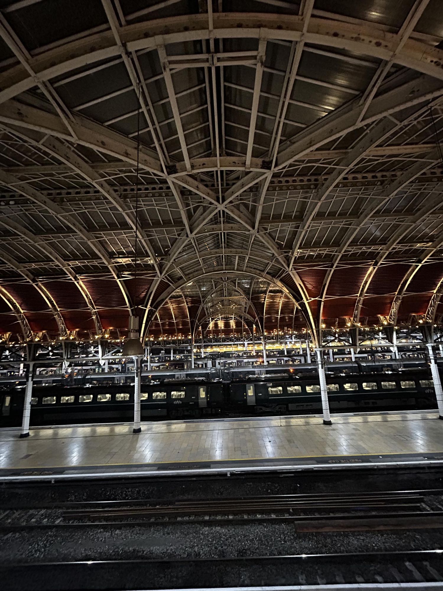 View of across the station at Paddington at night with a few trains in the station and the station lit up for the evening 