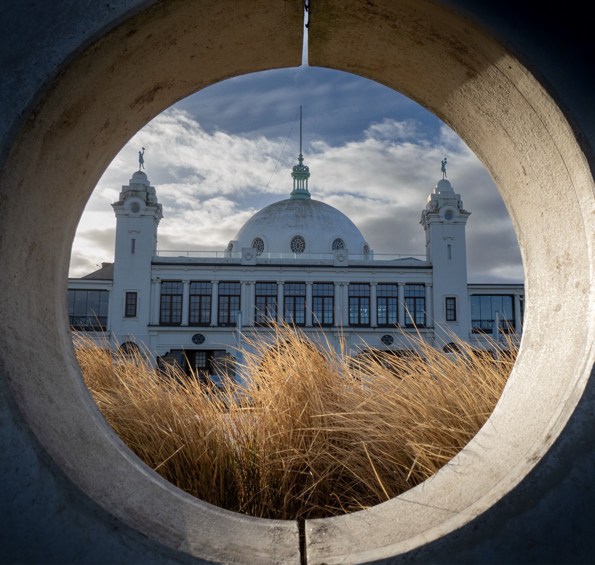 A photo taken through a concrete porthole of a white civic building with a dome roof.