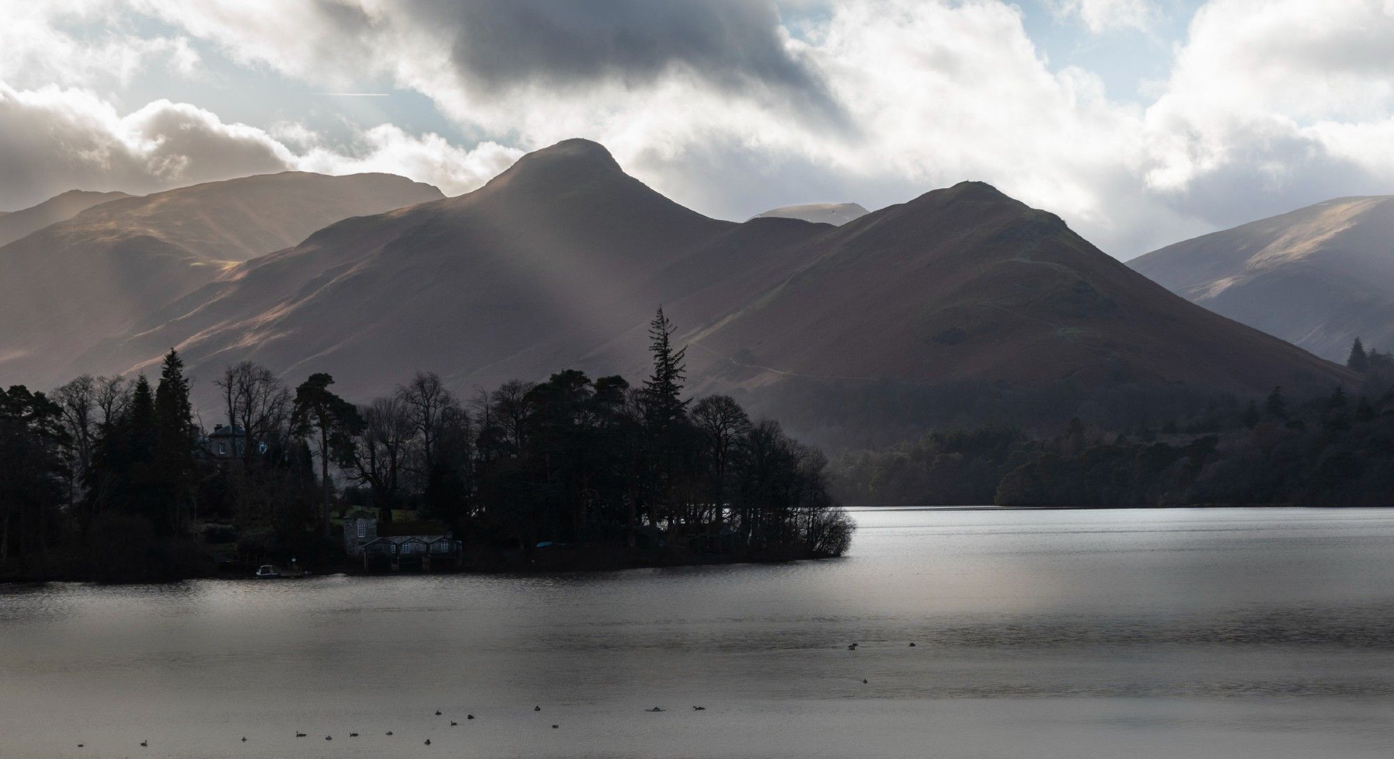 Beams of sunlight catch on a mountain ridge behind a a lake on a cloudy day