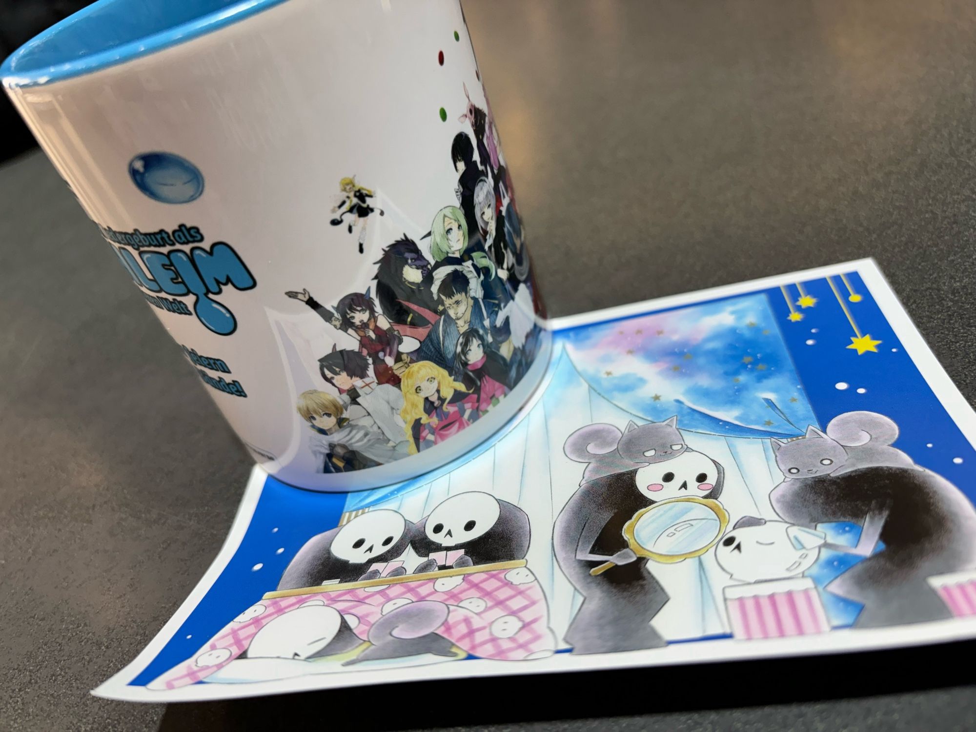 Eine Tasse und eine Postkarte jeweils mit Mangafiguren verziert auf einem Tisch