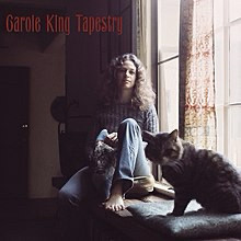 Cover for the album Tapestry by Carole King. She is sat in a window barefooted with a cat nearer to the camera.