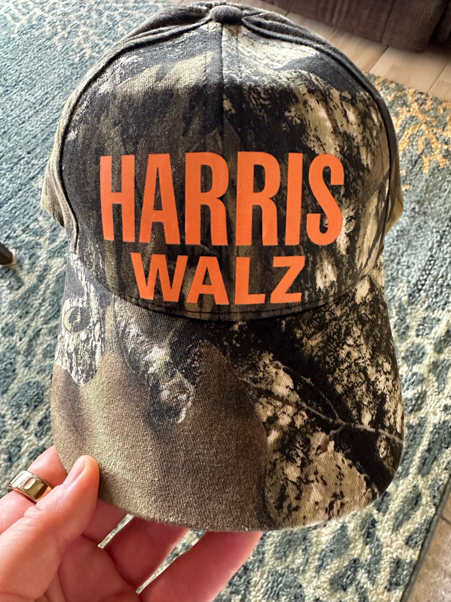 Camo colored baseball cap with “Harris Walz” printed in orange on the front