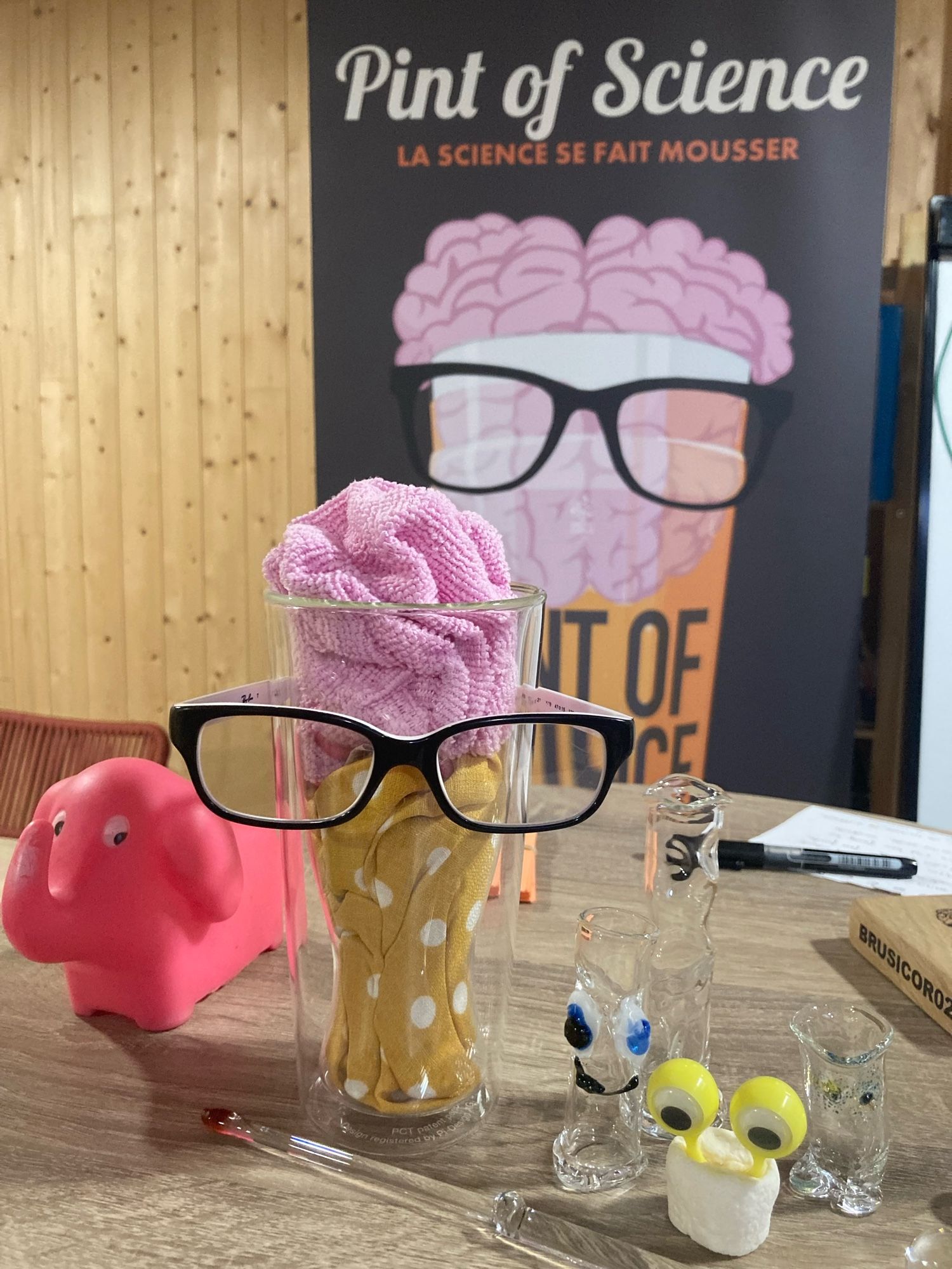 Affiche du festival Pint of Science avec en premier plan un verre avec du tissu dedans imitant de la bière et un cerveau, verre qui porte une paire de lunettes (je sais ça fait un peu ésotérique comme ça mais c’est pas simple à décrire)