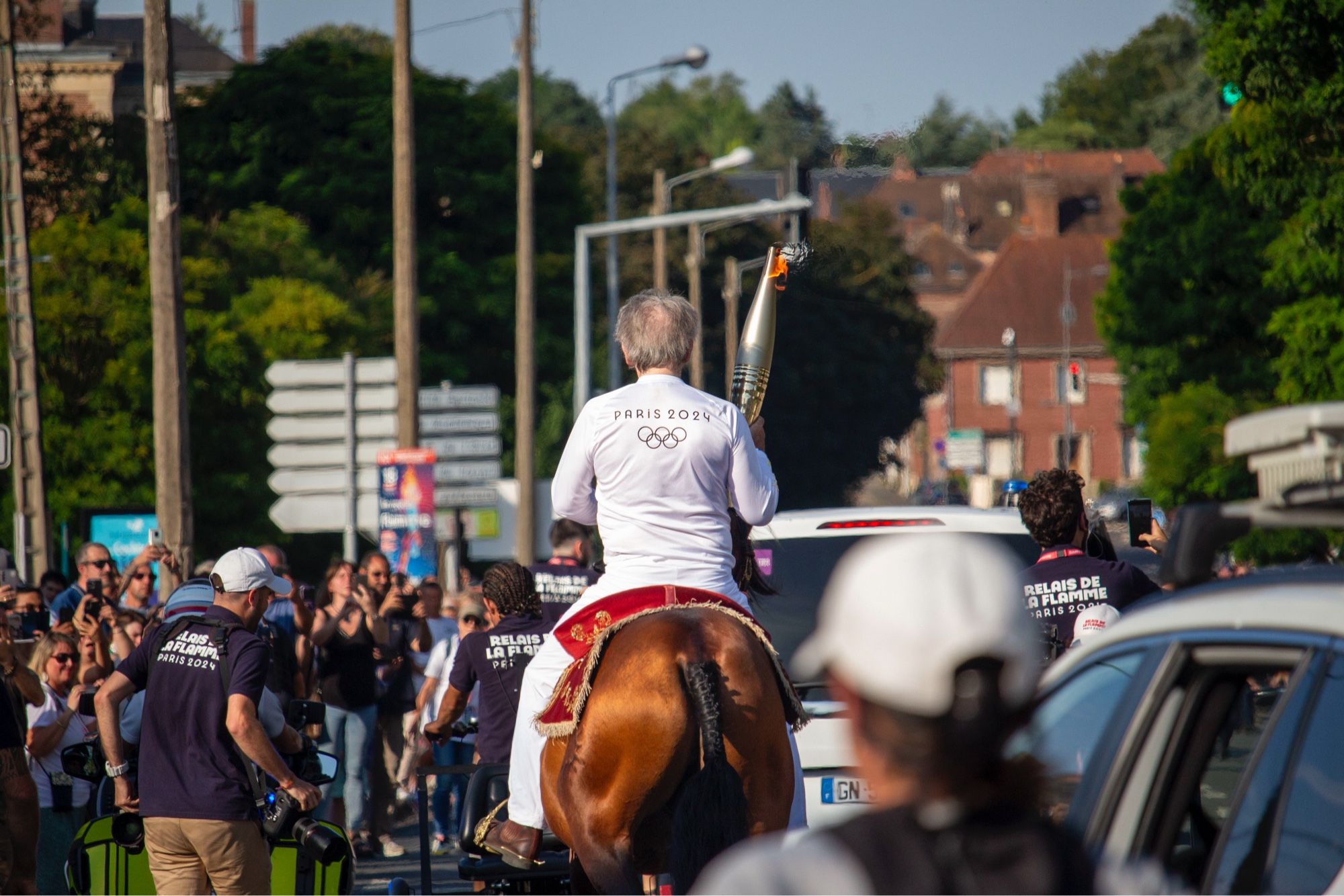 Porteur de flamme olympique à cheval, vu de dos.