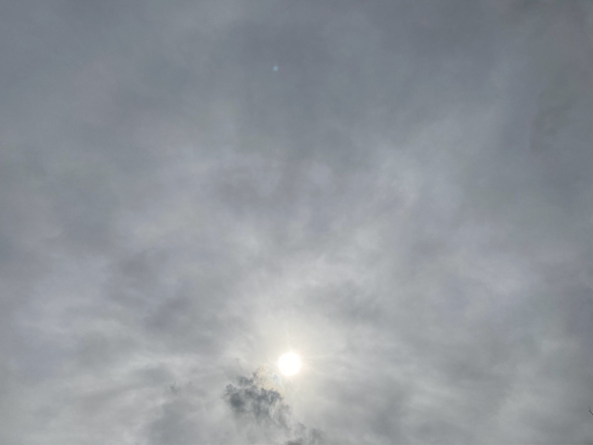 Die Sonne scheint durch die graue Wolkendecke. Gewellt strahlenförmiges Licht.