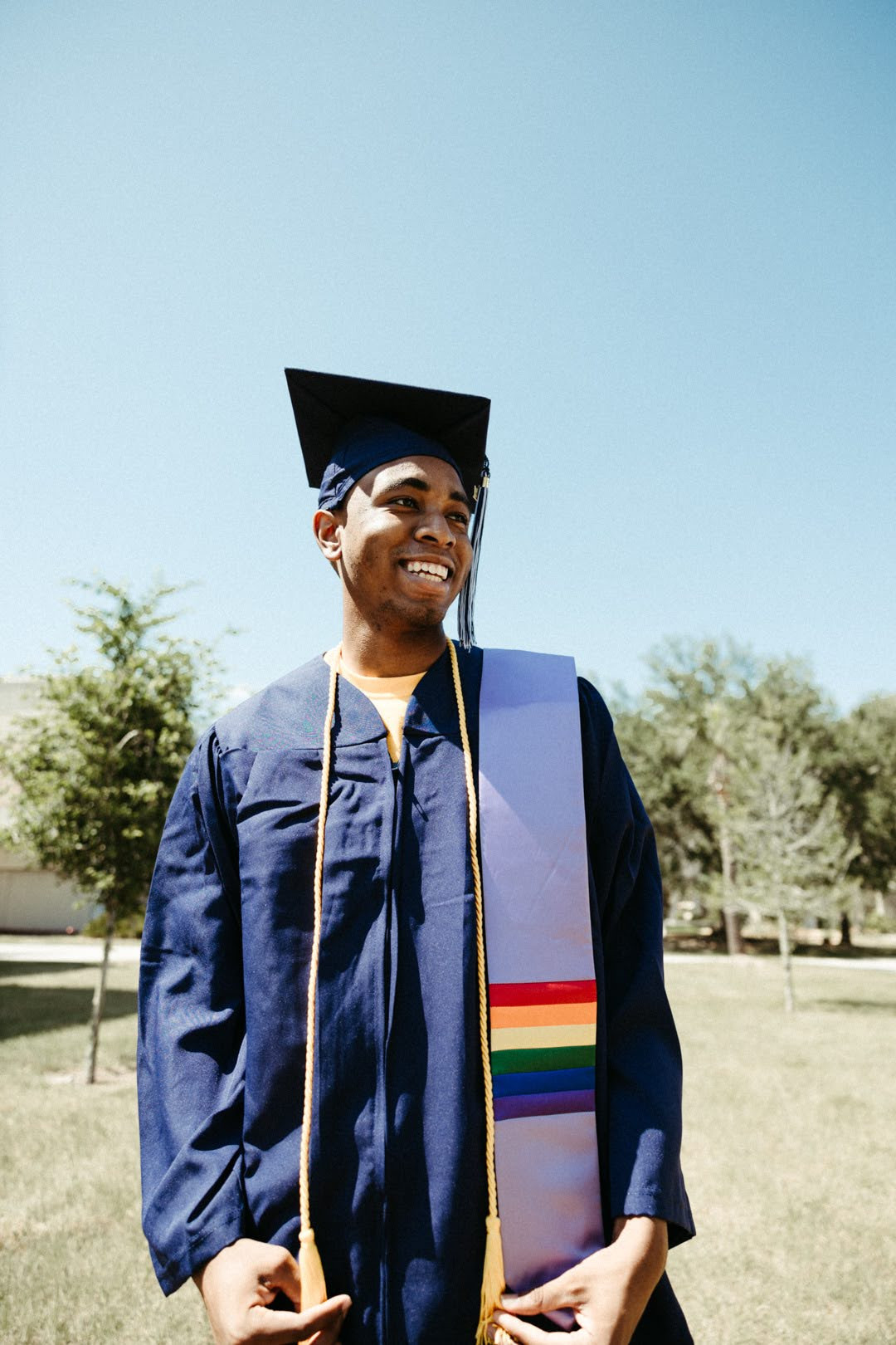 Napo standing and smiling in a graduation gown with pride stole