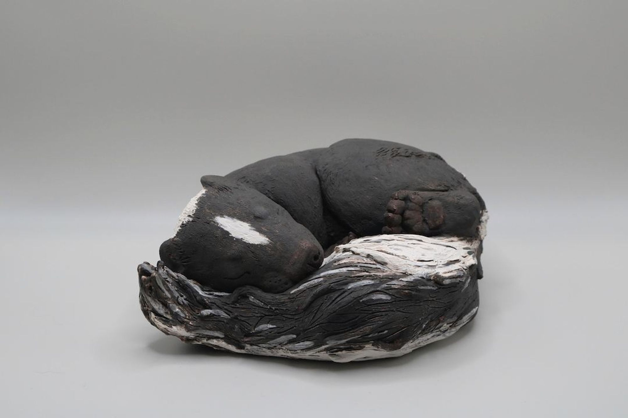 A ceramic sculpture of a striped skunk sleeping