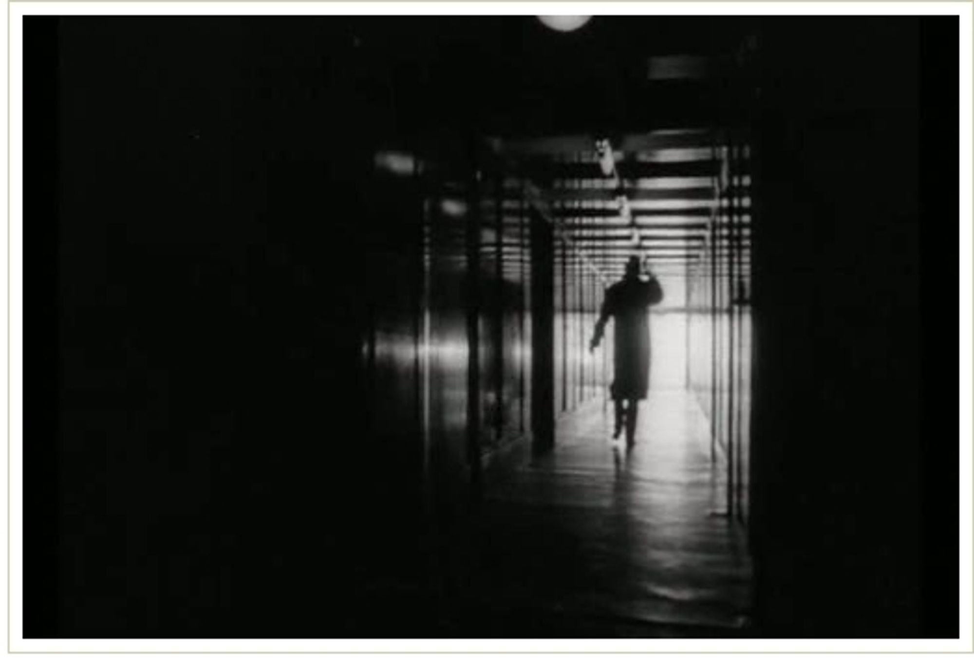 Classic image of a long, dark corridor with light at the bottom illuminating a man hurrying down the corridor holding on to his hat